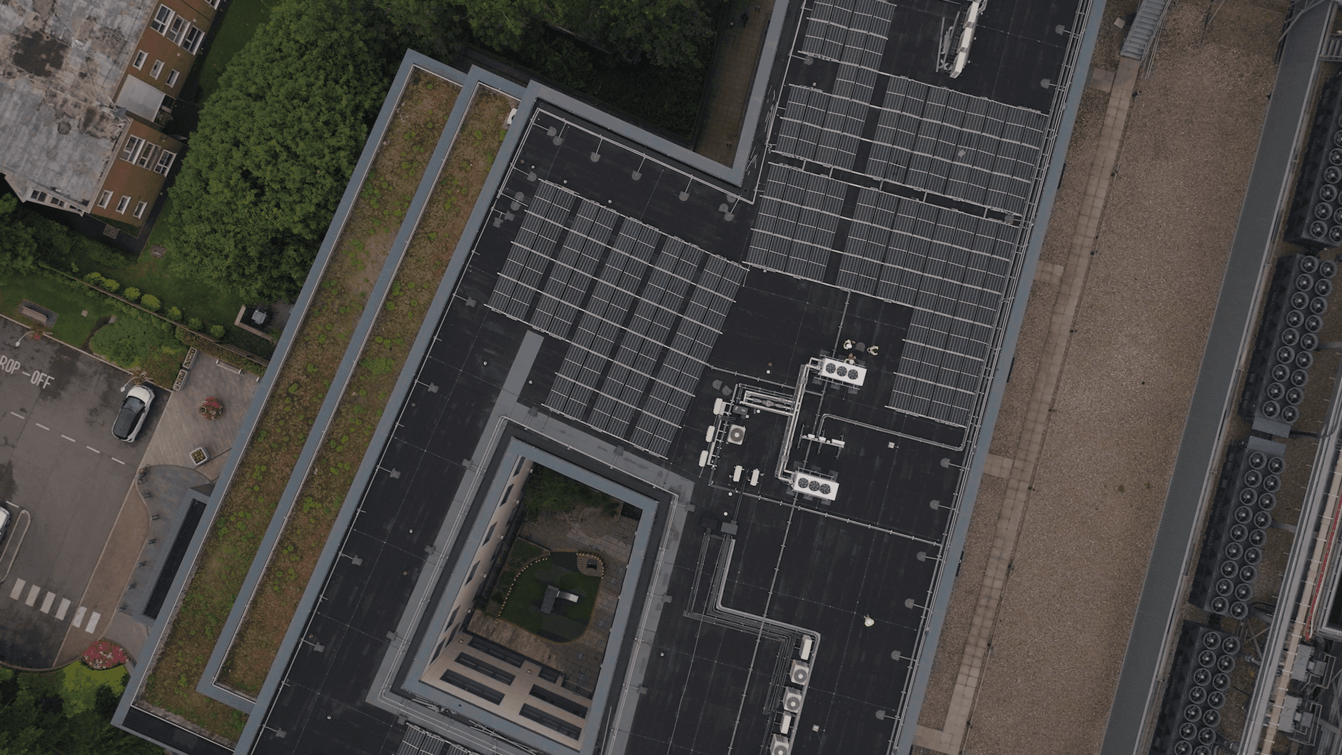 Luchtbeeld van een plat dak met rijen zonnepanelen en een groene dakrand