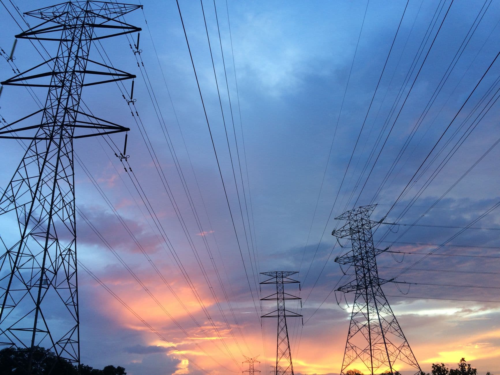 Hoogspanningsmasten en stroomkabels tegen een kleurrijke lucht bij zonsondergang