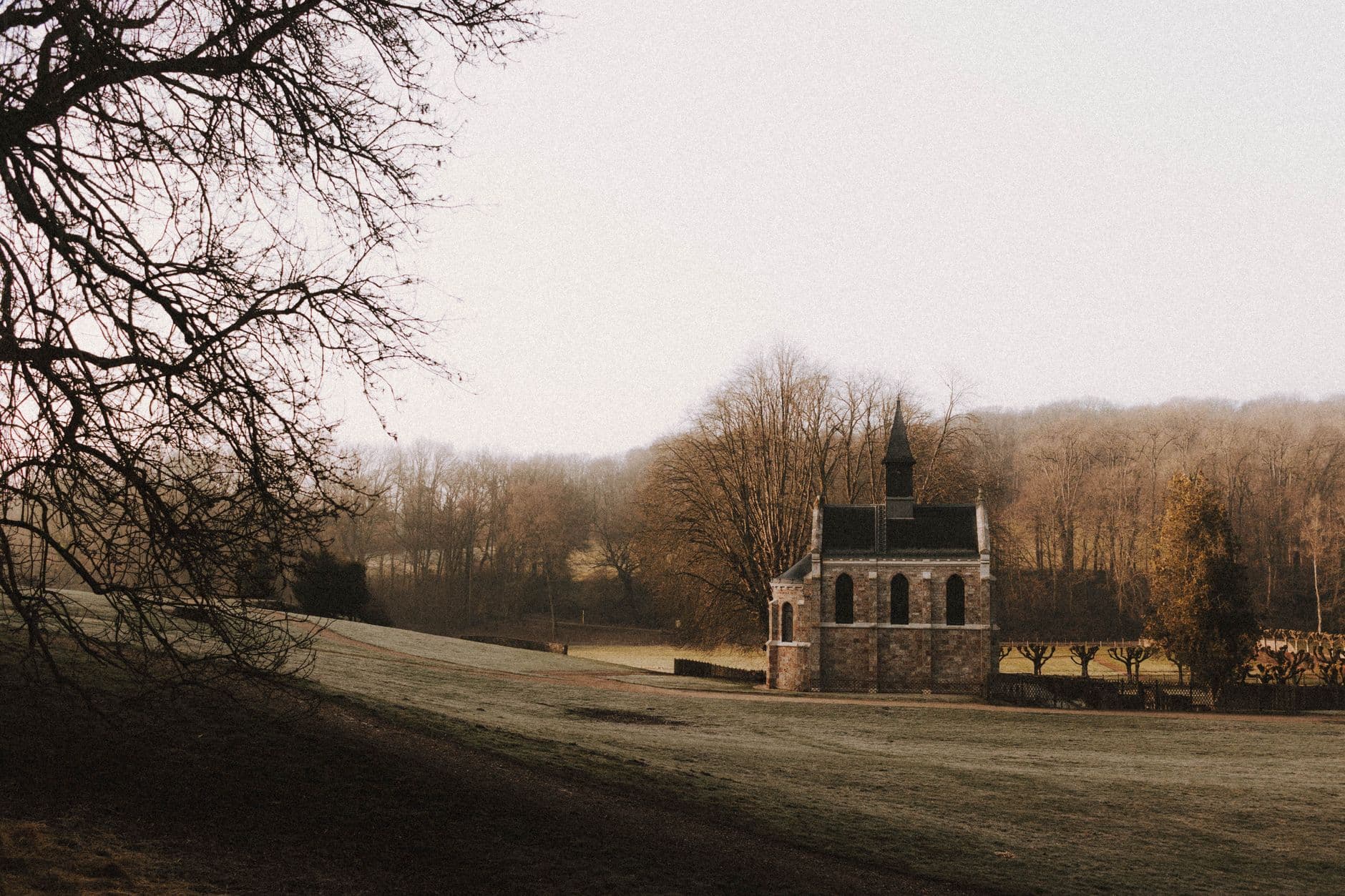 Neogotische stenen kapel op een grasveld tussen kale bomen in ochtendnevel