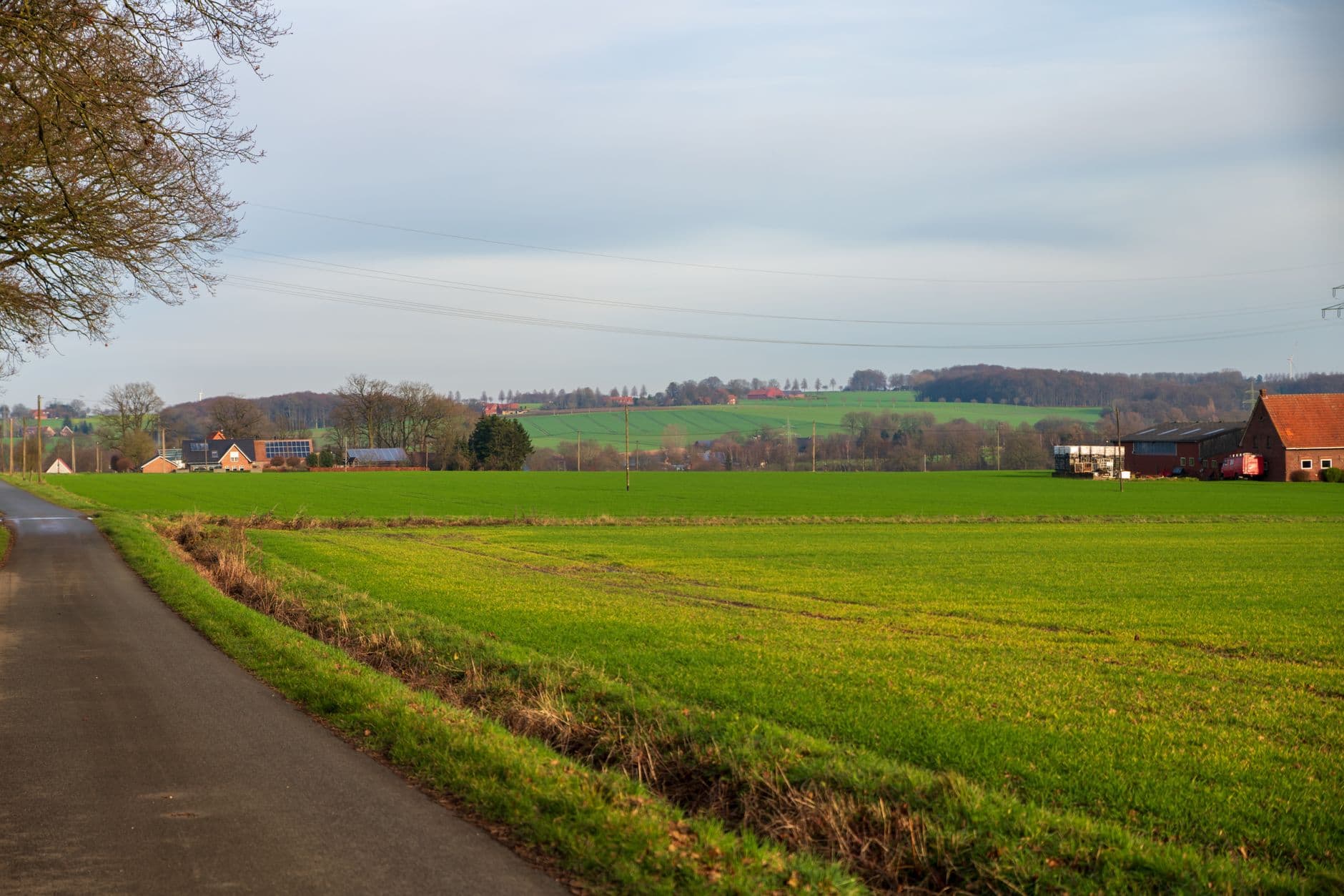 Landweg langs groene akkers met een bakstenen boerderij en glooiende velden in de verte
