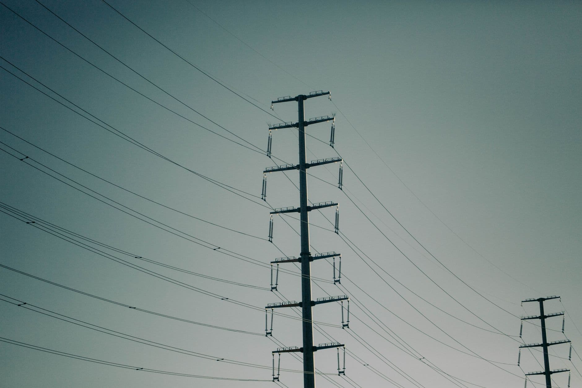 Hoogspanningsmasten met lange geleiders tegen een grijsblauwe lucht