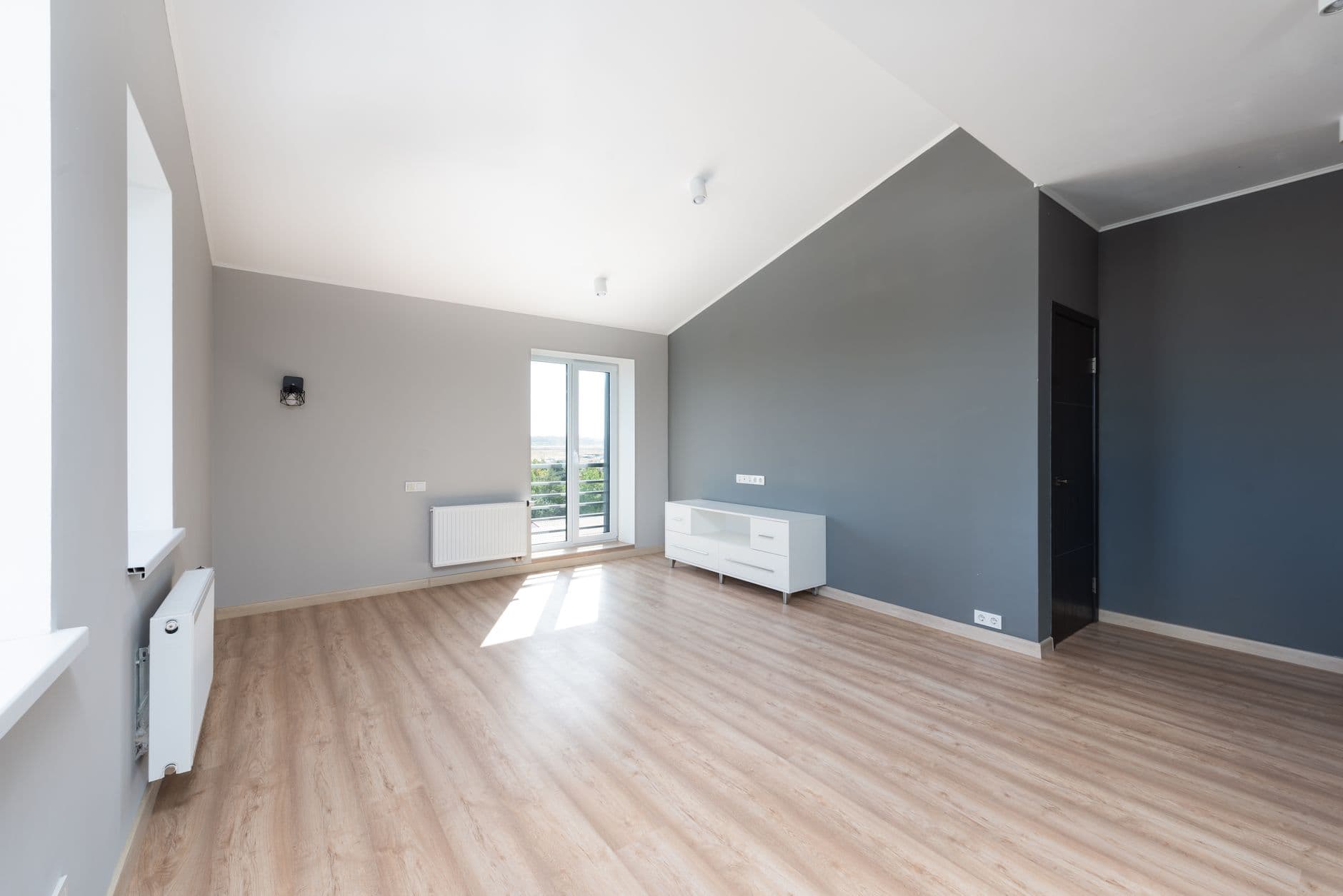 Lege, lichte kamer onder een schuin dak met grijze wanden, laminaatvloer en radiatoren