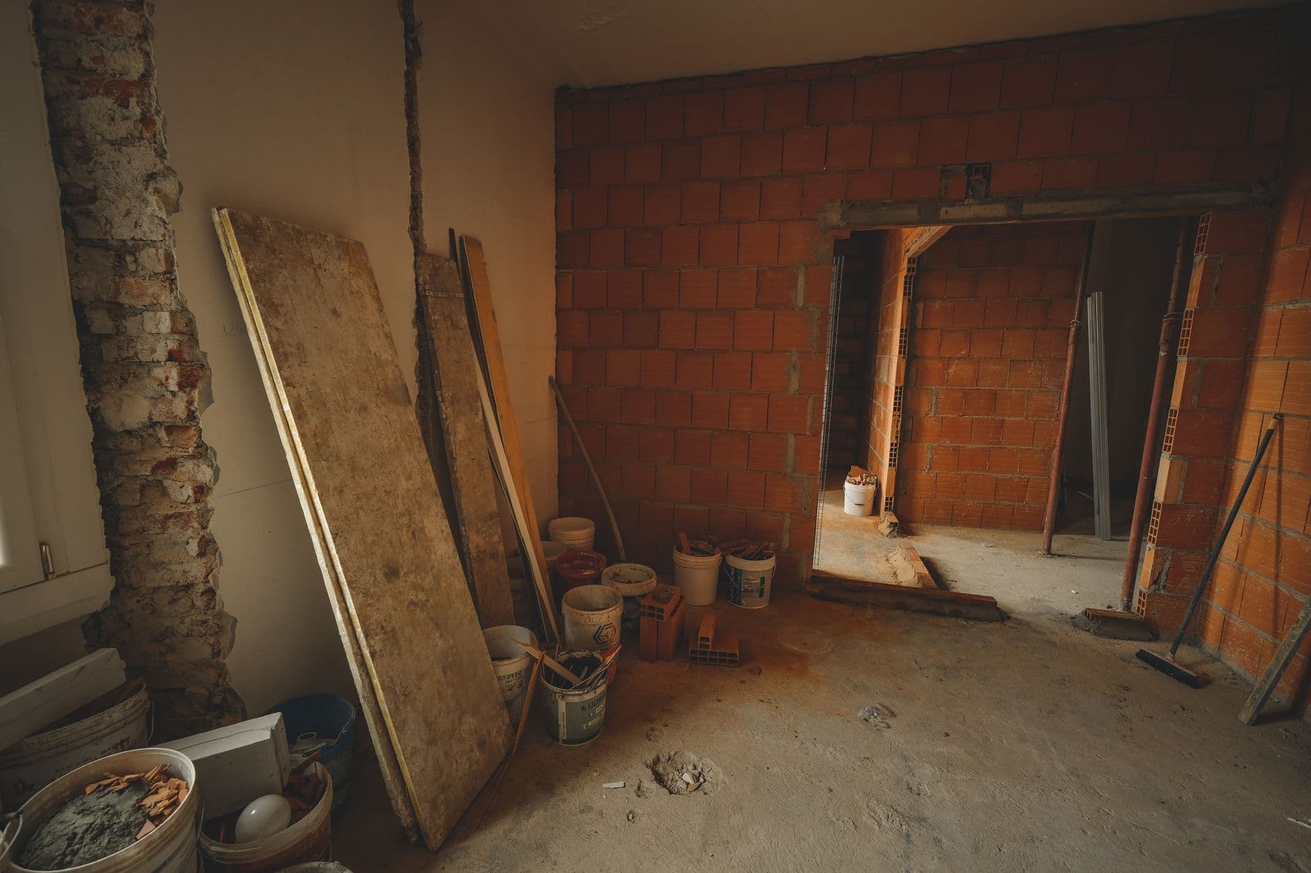 Kamer in renovatie met bakstenen muren, platen en emmers met bouwmateriaal op de vloer