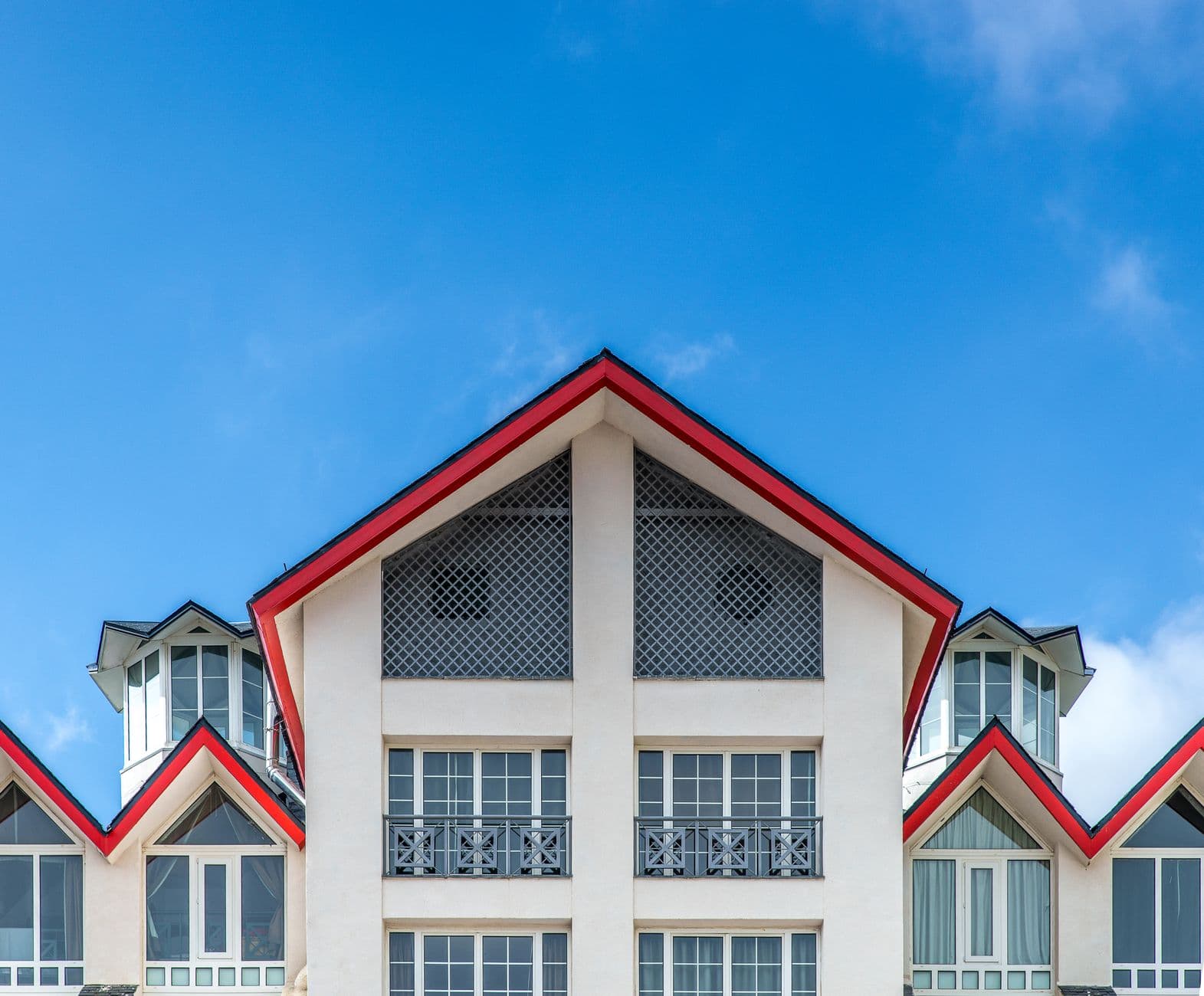 Witte gevel met rood afgewerkte puntgevels, erkers en smeedijzeren balkons onder een blauwe lucht
