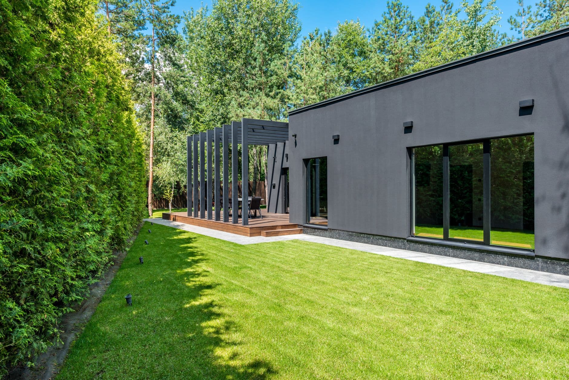 Modern donker gelijkvloers huis met pergola en groot gazon tussen dennenbomen