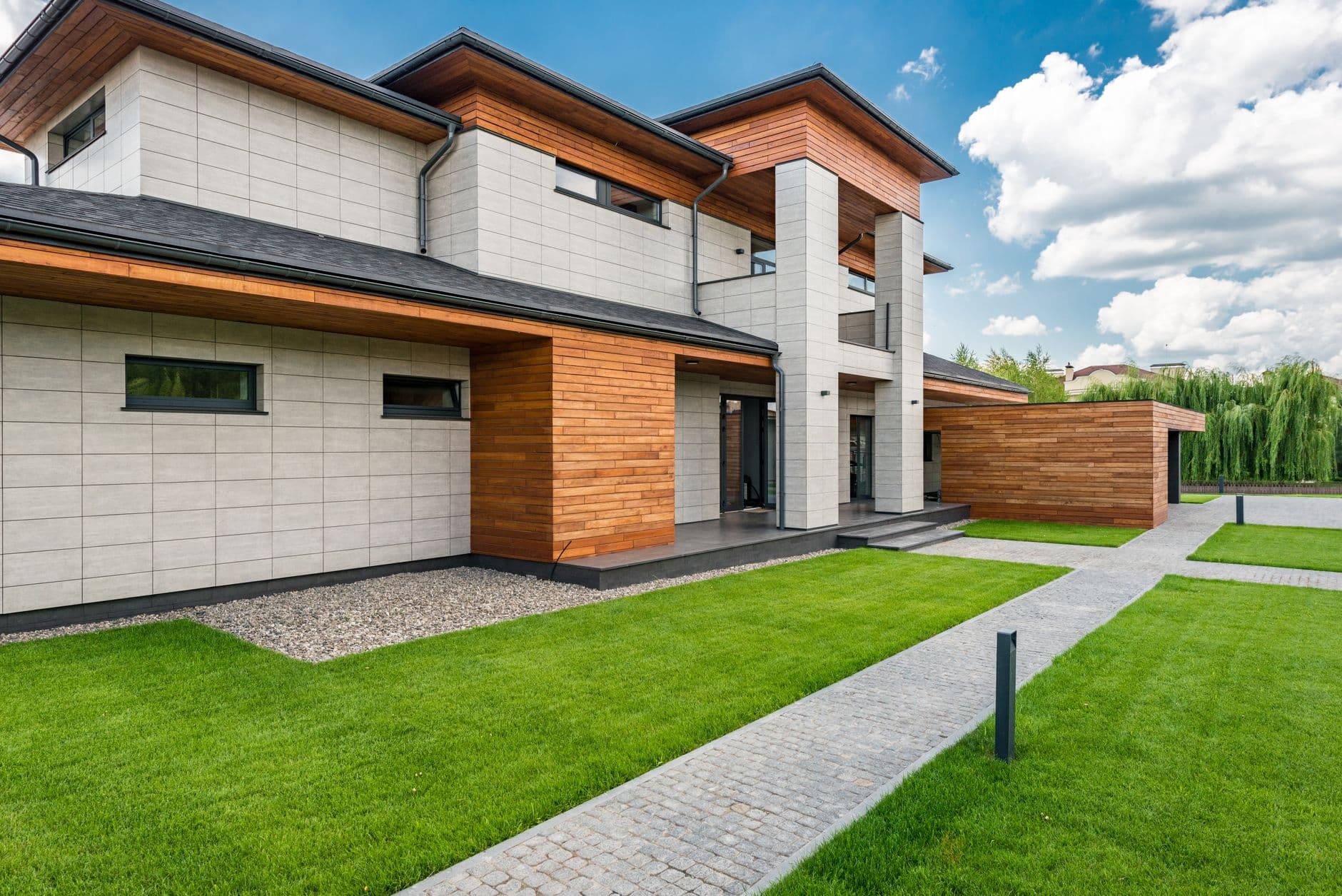 Moderne woning met houten gevelaccenten, grasveld en een wilg op de achtergrond