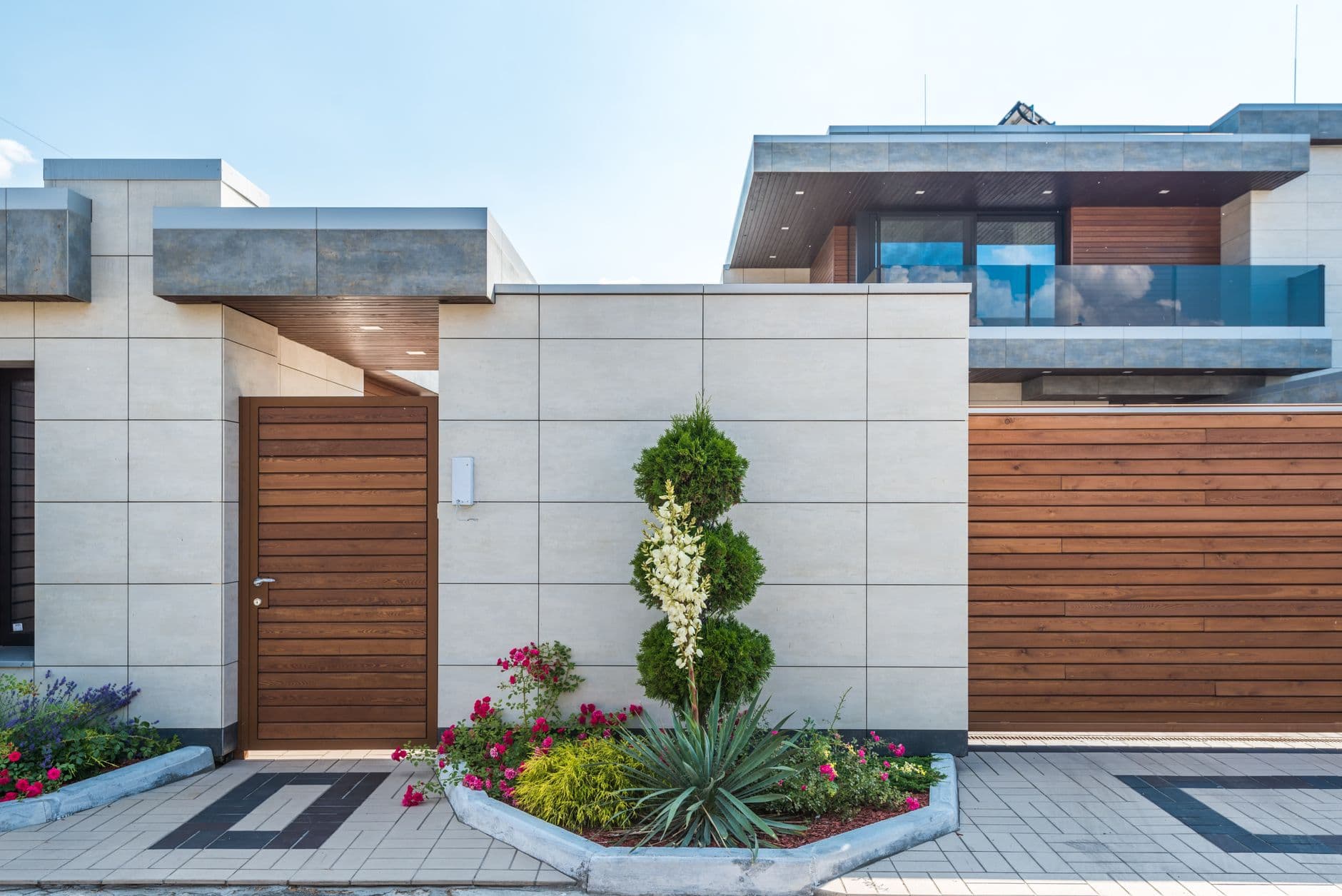 Moderne woning met lichte gevelplaten, houten poort en garagepoort achter een bloeiende border