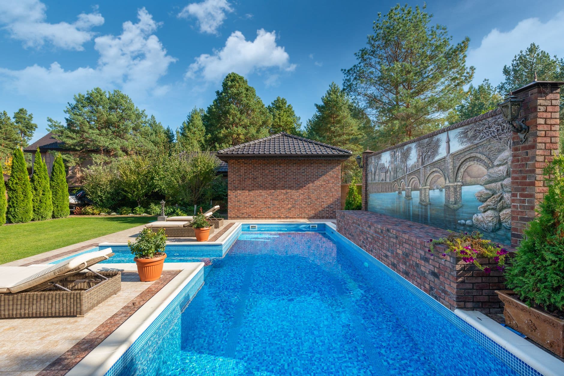 Tuin met zwembad, terras en een bakstenen poolhouse tussen hoge dennen en coniferen