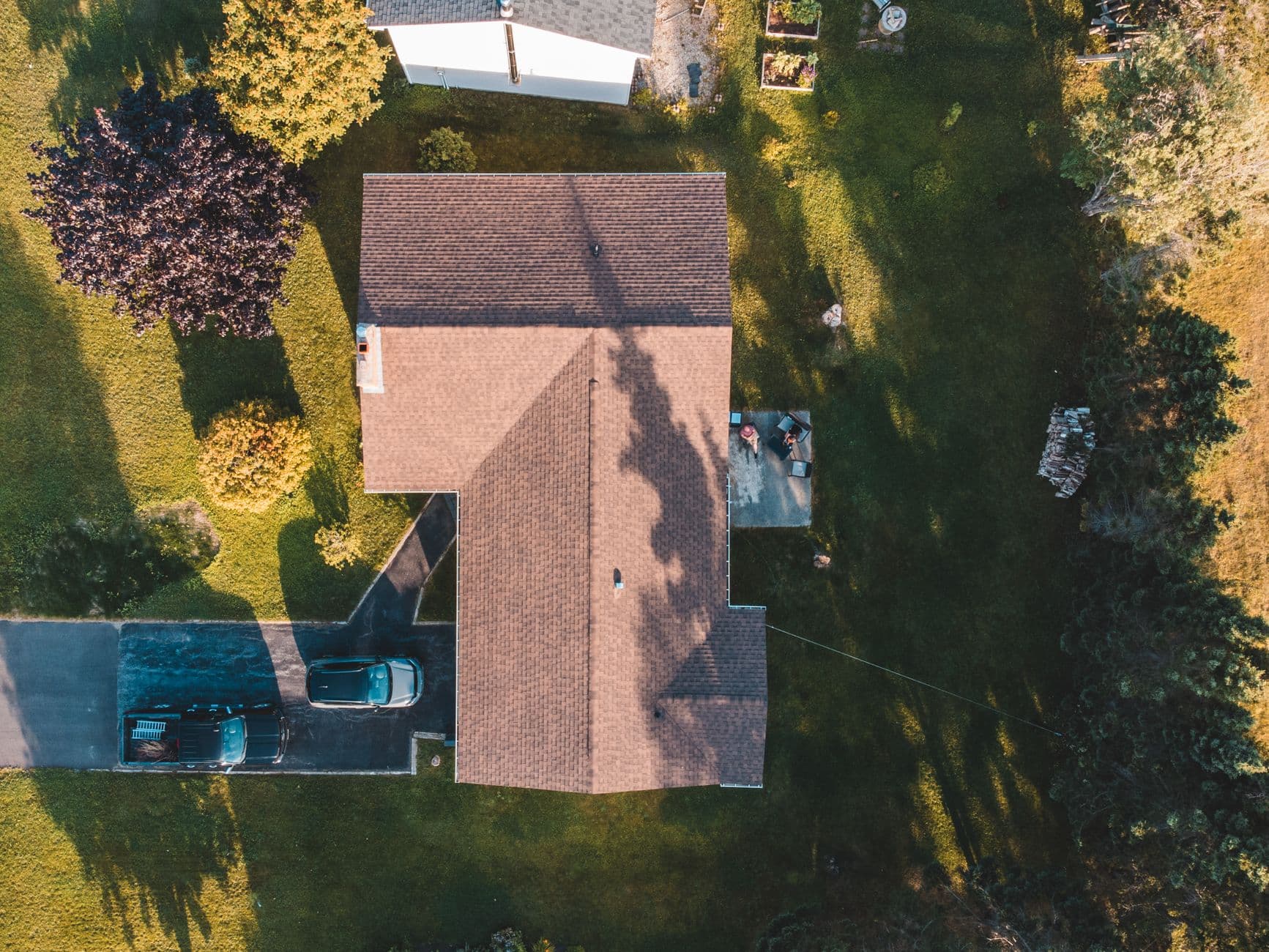 Luchtbeeld recht van boven op een vrijstaande woning met ruime grasvelden en twee geparkeerde auto's