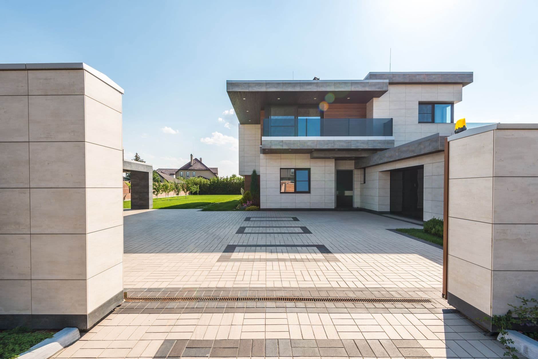 Oprit van gebakken klinkers naar een moderne villa met glazen balkon en lichte gevelbekleding