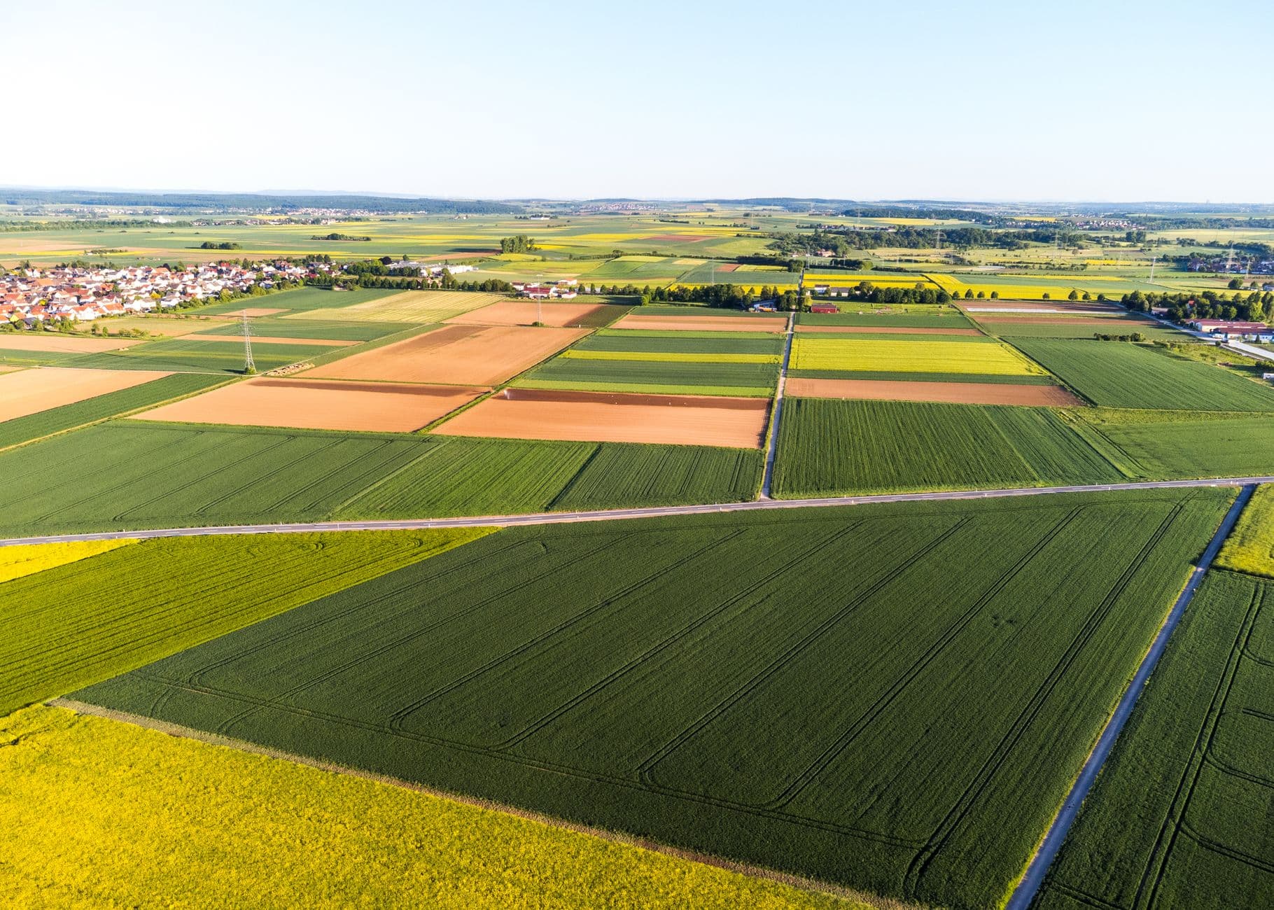 Luchtbeeld van akkers in een lappendeken met aan de rand een dorp met rode daken