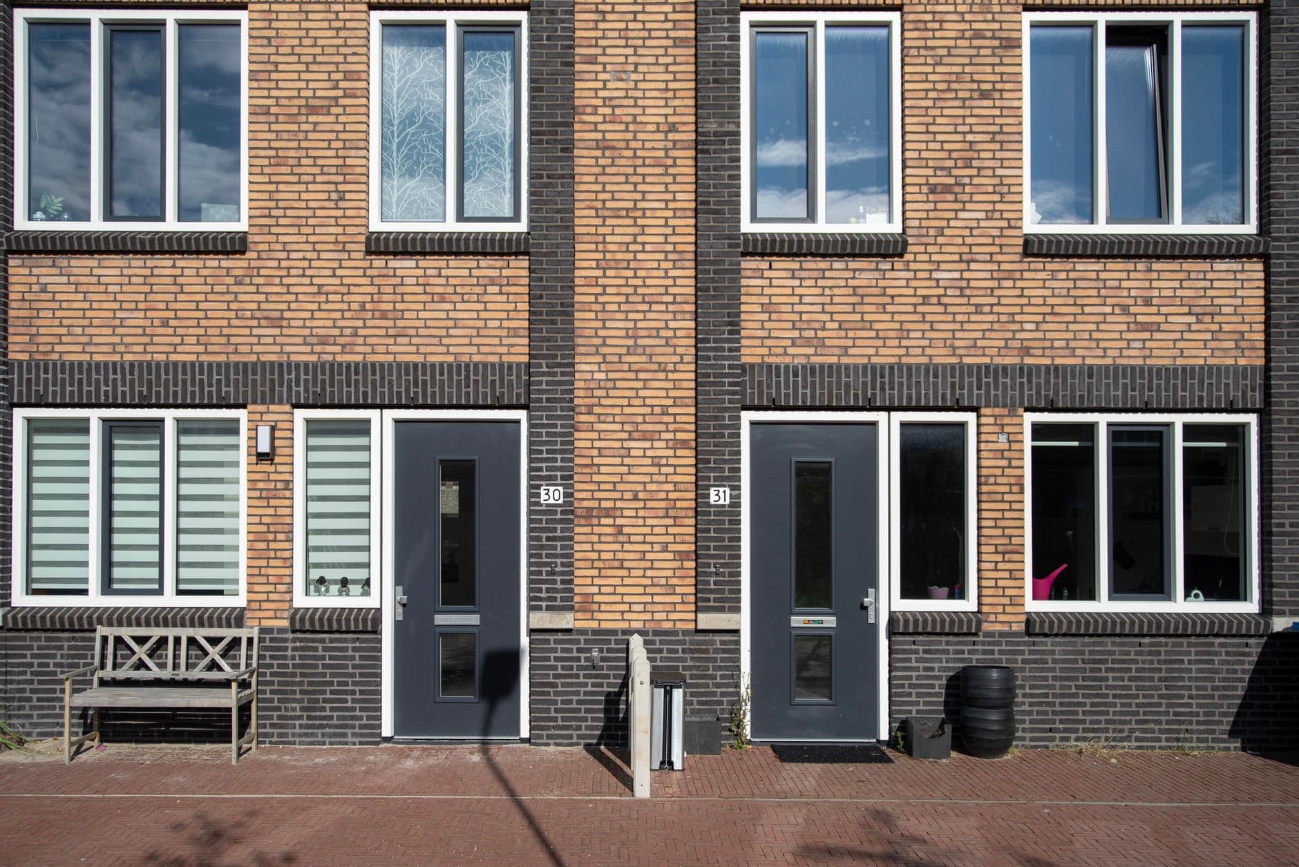 Gevel van nieuwe bakstenen rijwoningen met grijze voordeuren en grote ramen