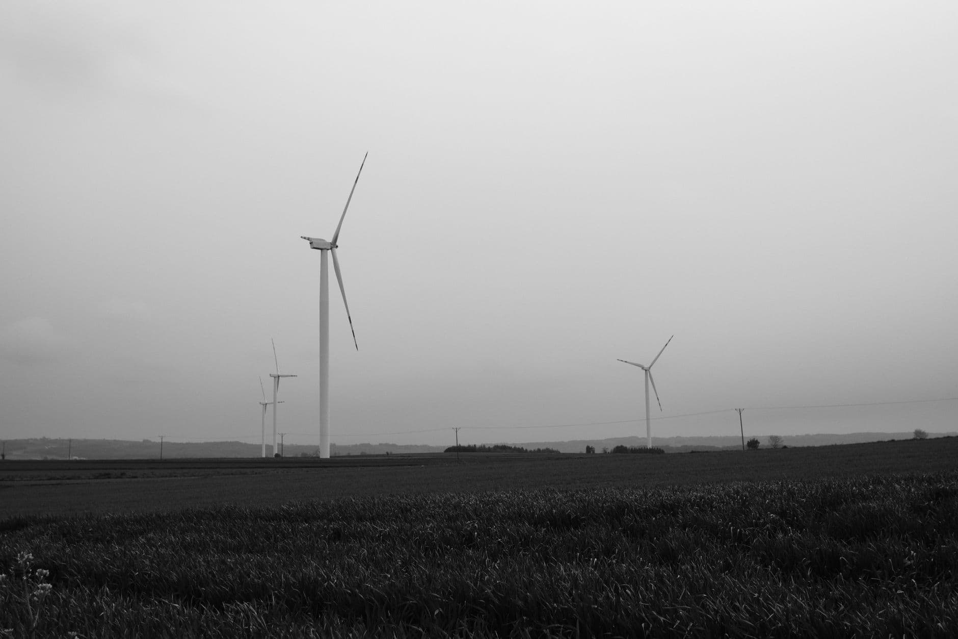 Zwart-witbeeld van windturbines boven een akkerveld onder een bewolkte lucht