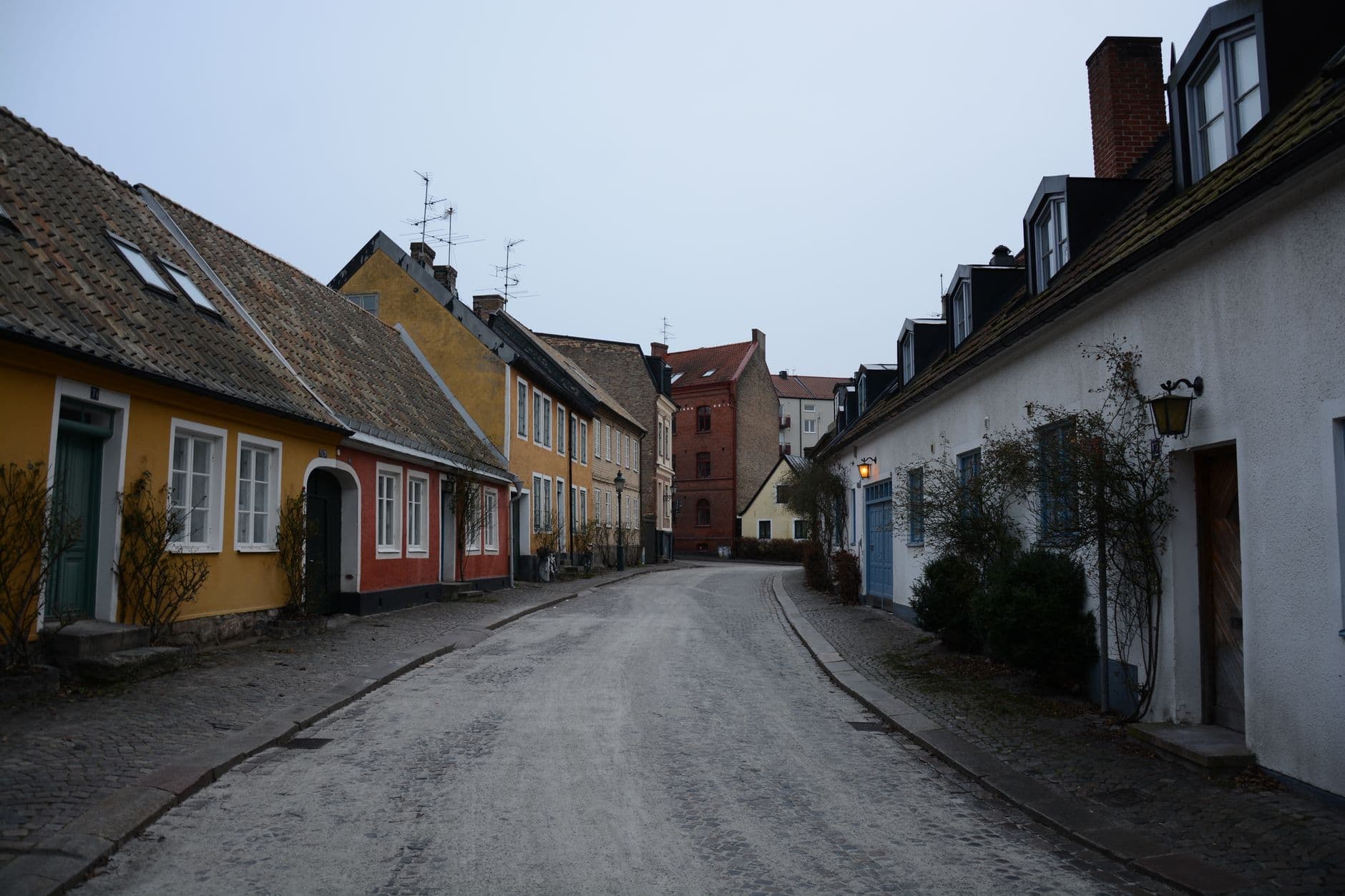 Kasseistraat met lage historische rijhuizen in gele, rode en witte gevels bij valavond