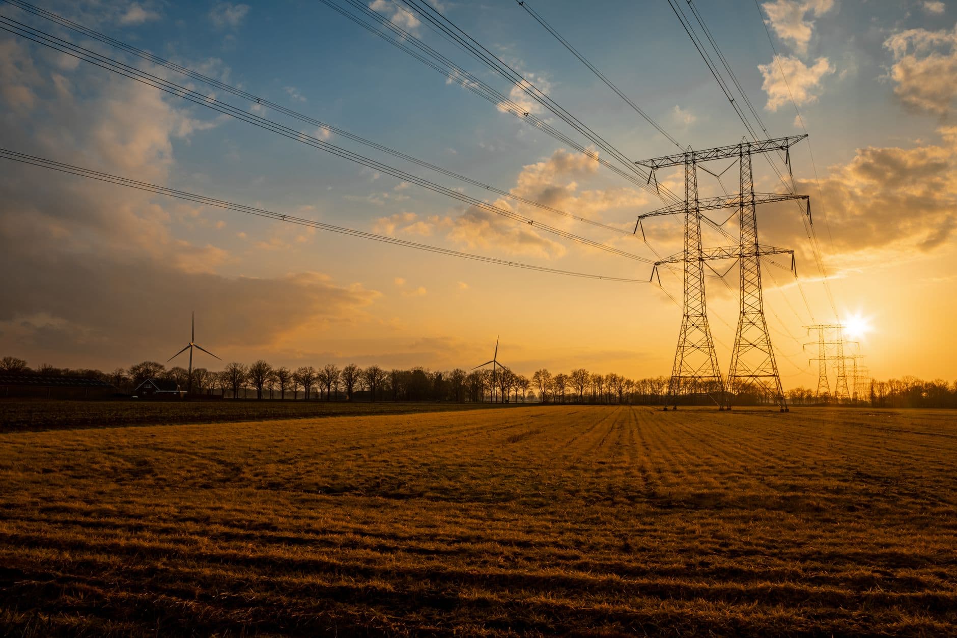 Hoogspanningsmasten en windturbines boven een geoogste akker bij zonsondergang