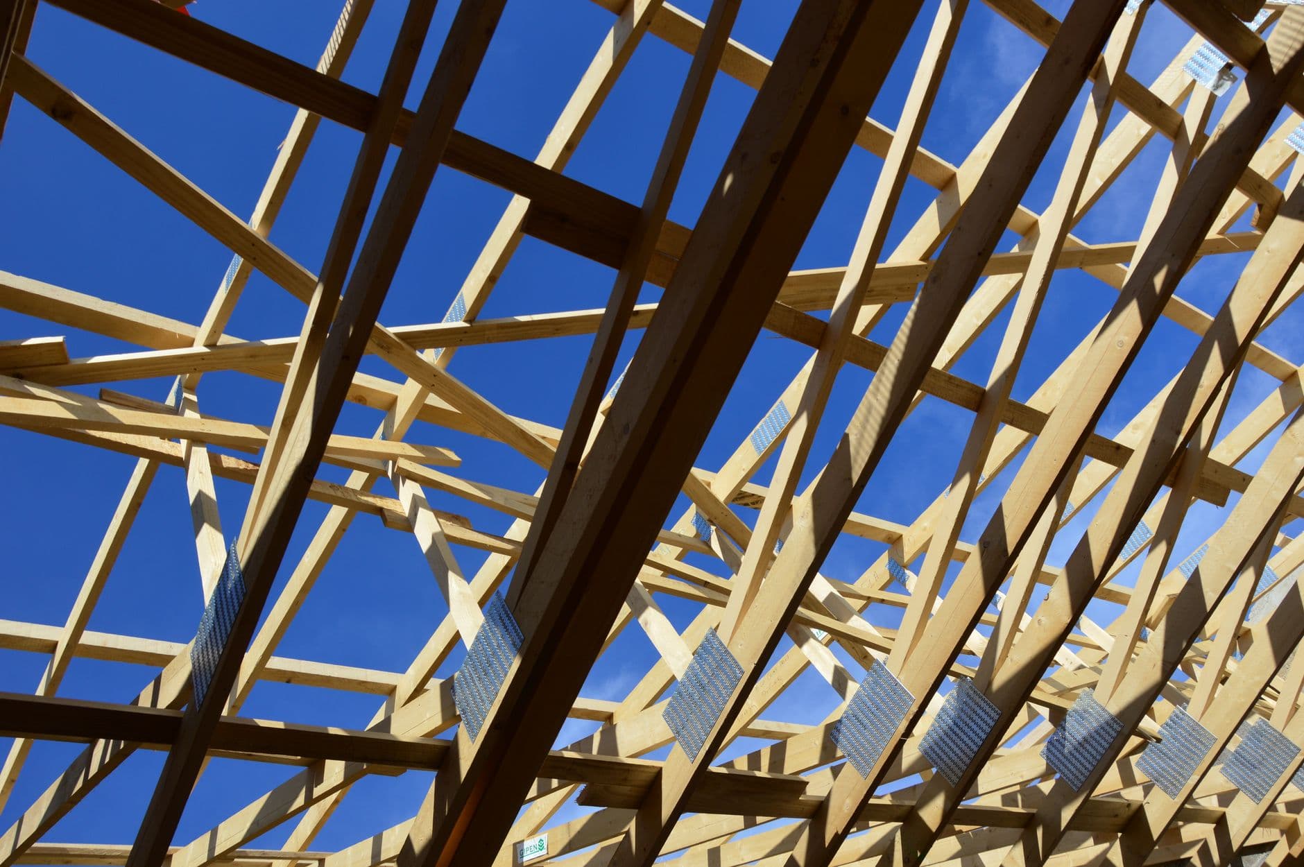 Houten dakspanten met metalen verbindingsplaten tegen een blauwe lucht tijdens de bouw van een dak