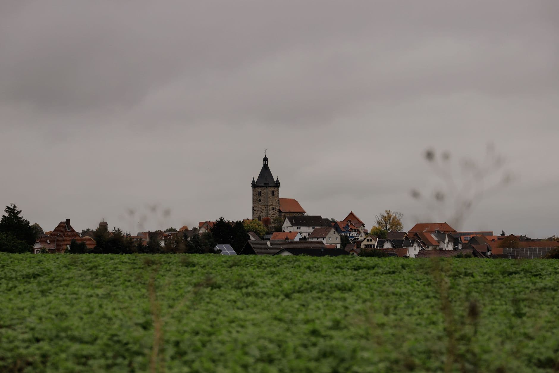 Dorp met kerktoren en zonnepanelen op de daken achter een groene akker onder een grijze wolkenlucht