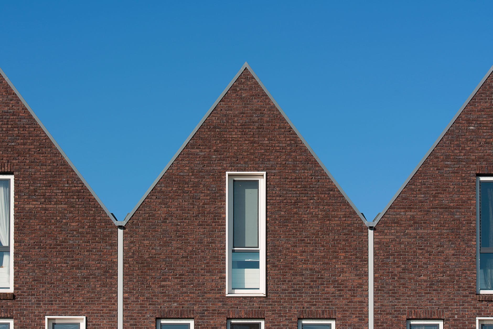 Drie puntgevels van rode baksteen met smalle ramen tegen een strakblauwe lucht