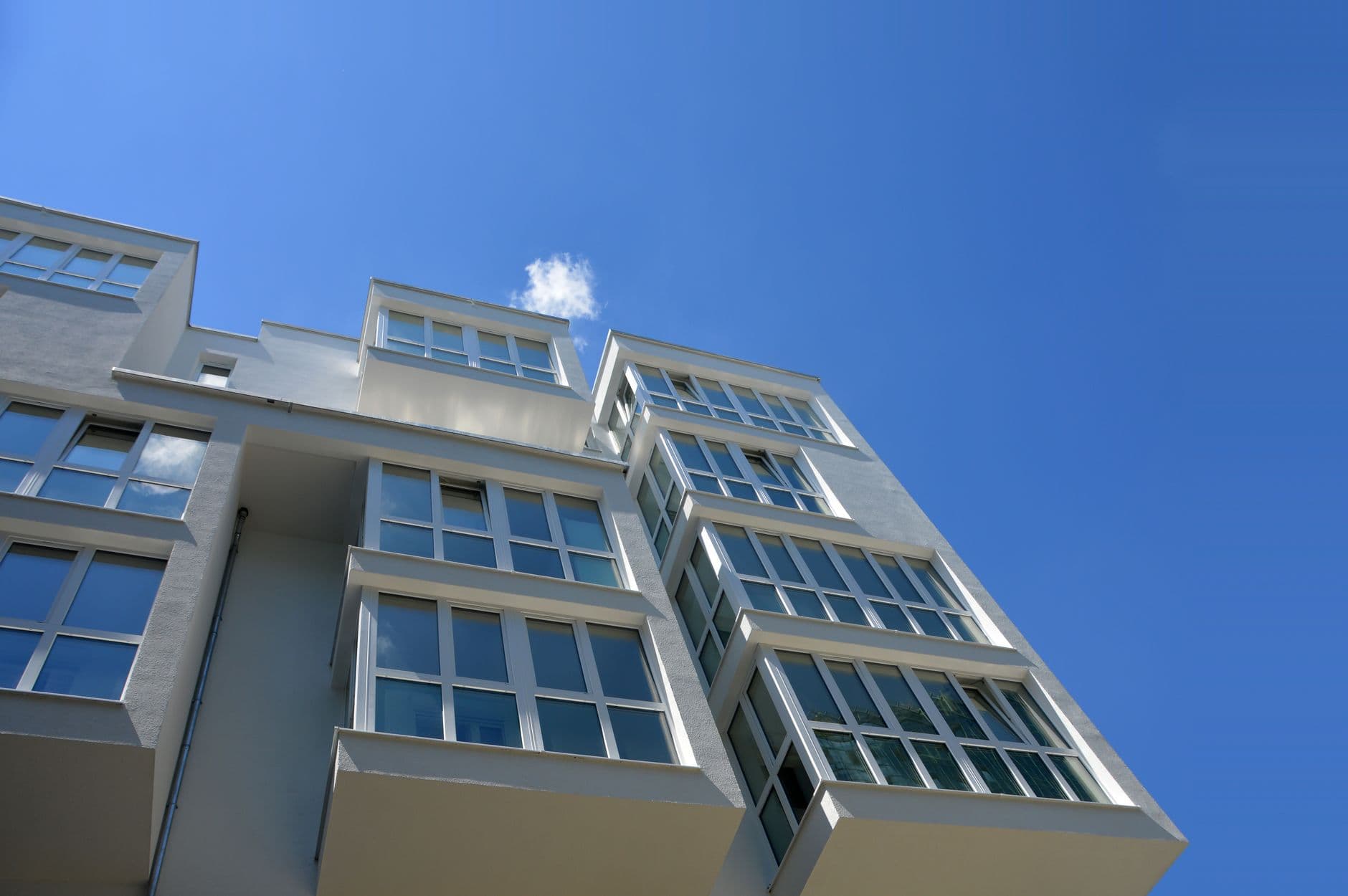 Wit appartementsgebouw met glazen erkers, van onderuit gezien tegen een blauwe lucht