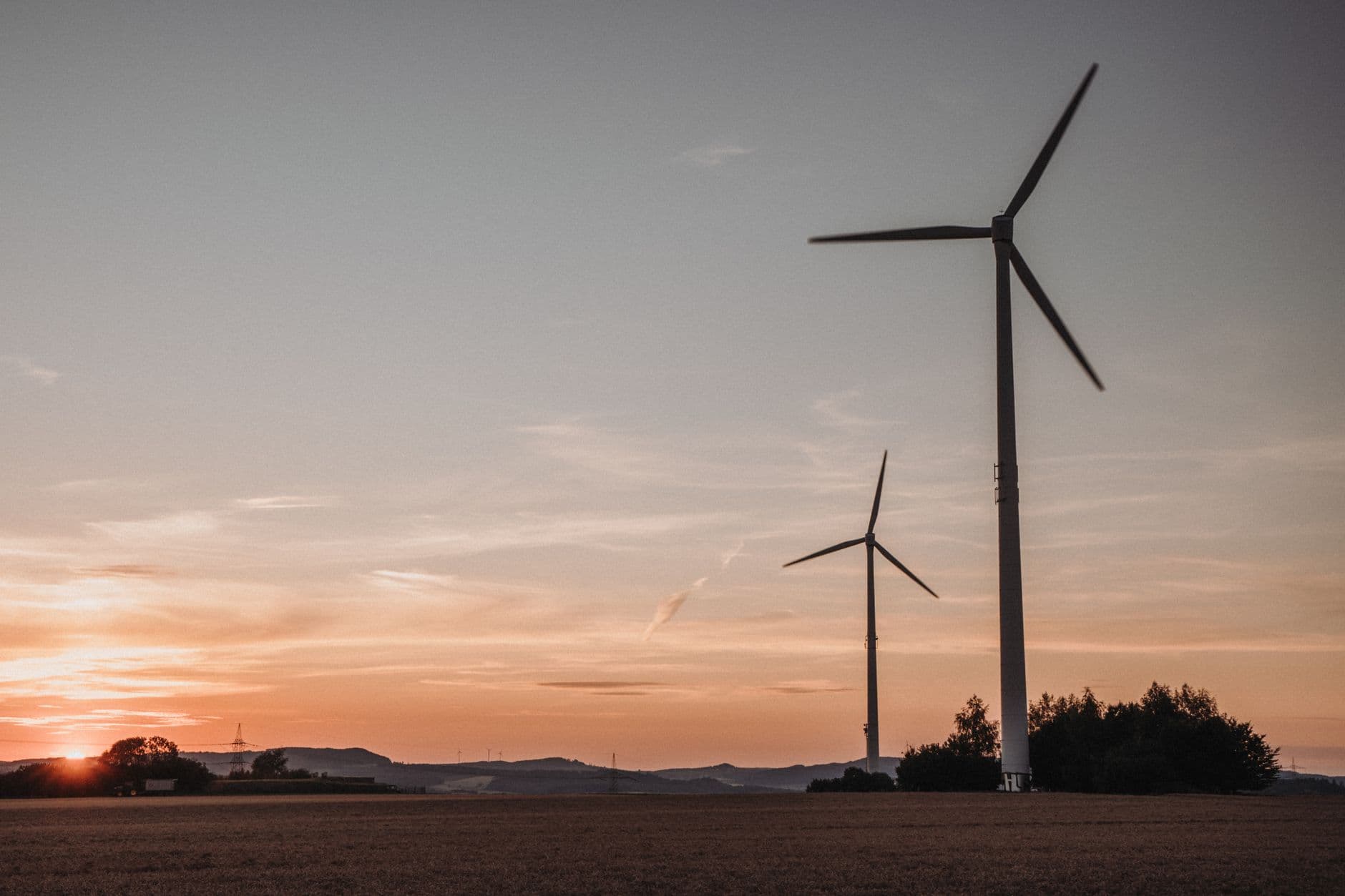 Windturbines boven een vlakke akker bij zonsondergang met een oranje avondlucht