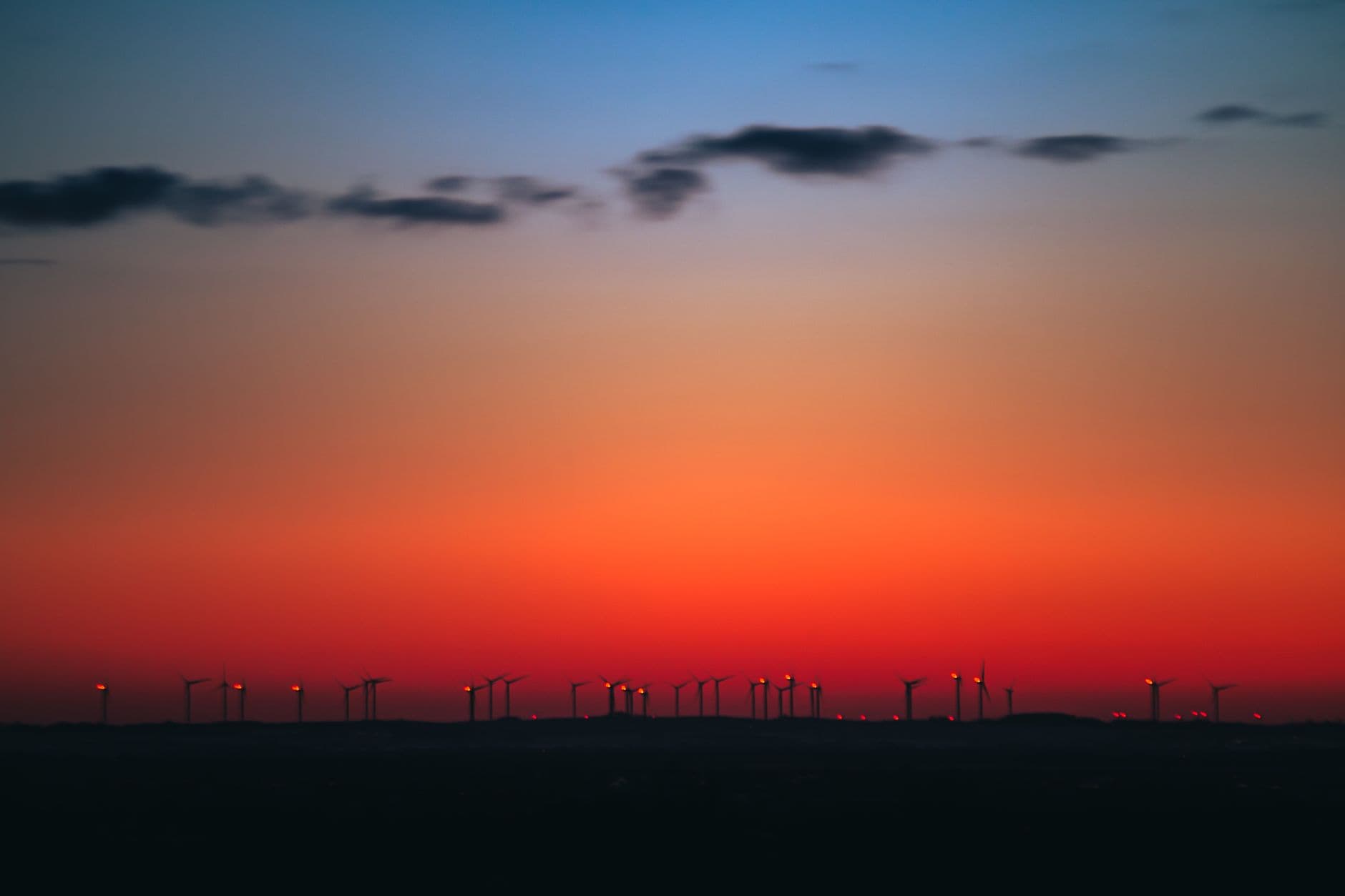 Rij windturbines als silhouet tegen een rode avondhemel boven een vlak landschap