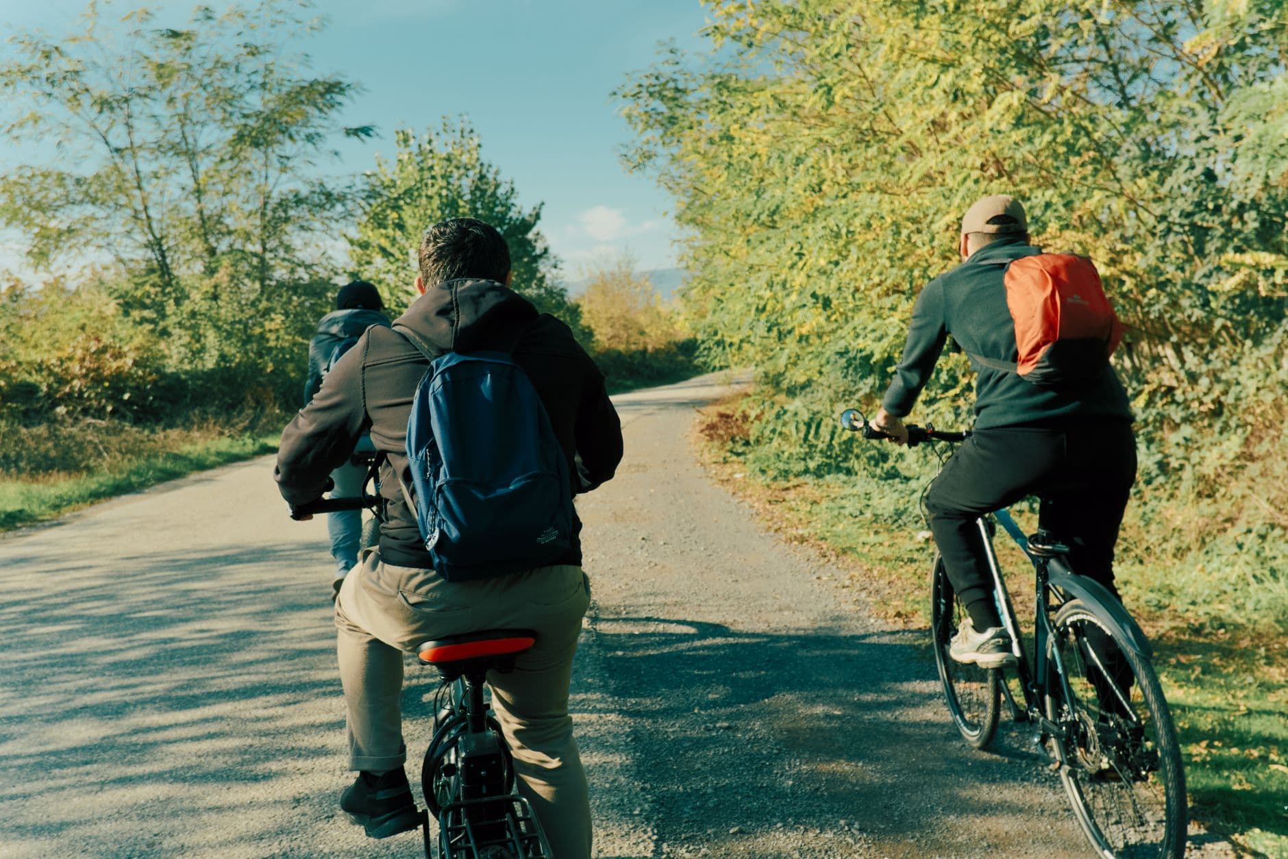 Drie fietsers van achteren op een grindpad tussen herfstig struikgewas onder een blauwe lucht