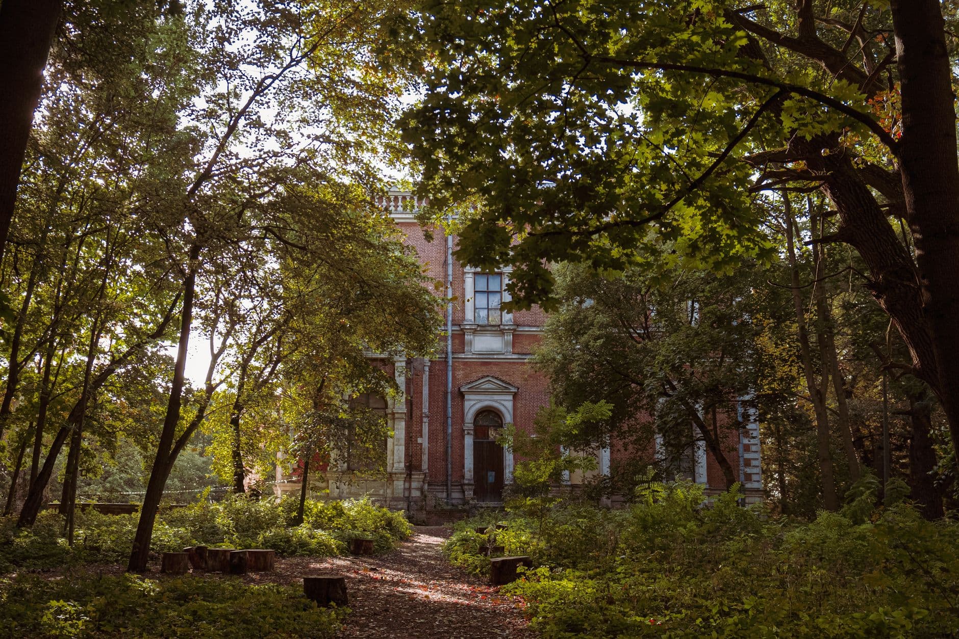 Oude bakstenen villa tussen hoge bomen en groen struikgewas in zacht zonlicht
