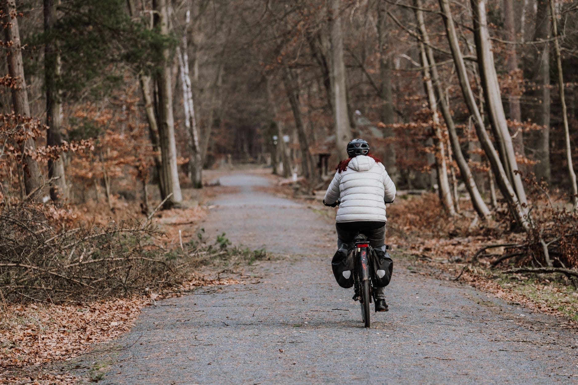 Fietser in winterjas op een bospad tussen kale bomen in de herfst, gezien van achteren