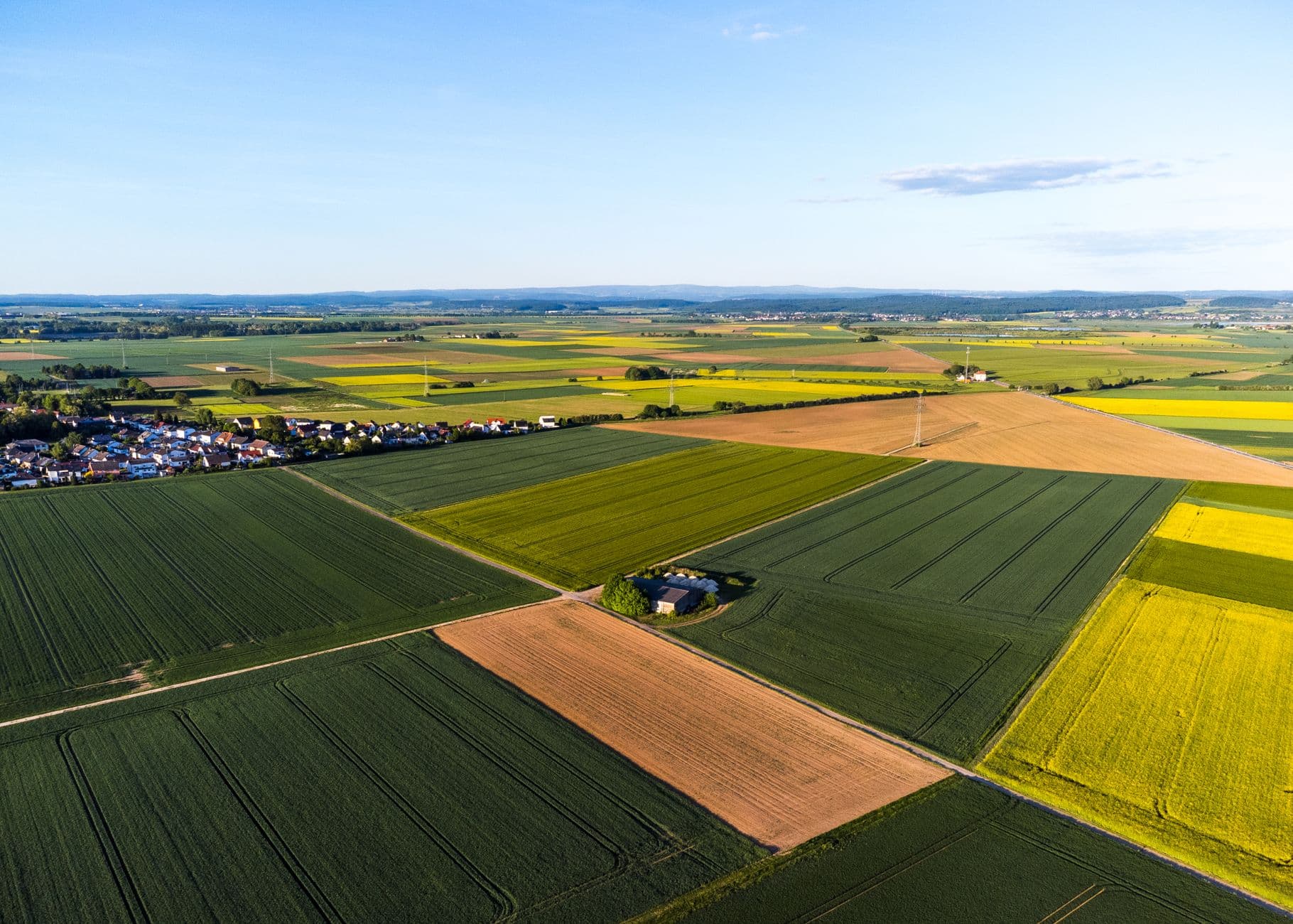 Luchtbeeld van groene akkers en gele koolzaadvelden met een dorpsrand in de verte