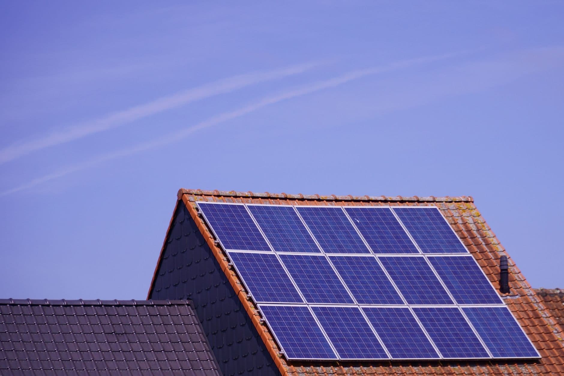 Zonnepanelen op een pannendak van een woning onder een blauwe lucht