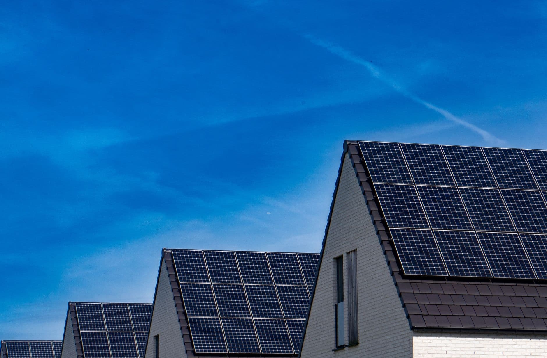 Rij nieuwbouwwoningen met zonnepanelen op de daken onder een blauwe lucht
