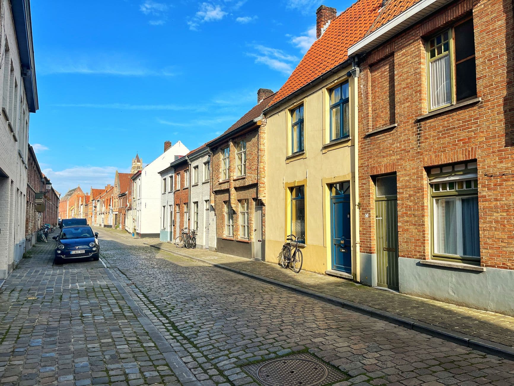 Maisons mitoyennes en briques dans une rue pavée de Bruges, avec vélos et voiture garée