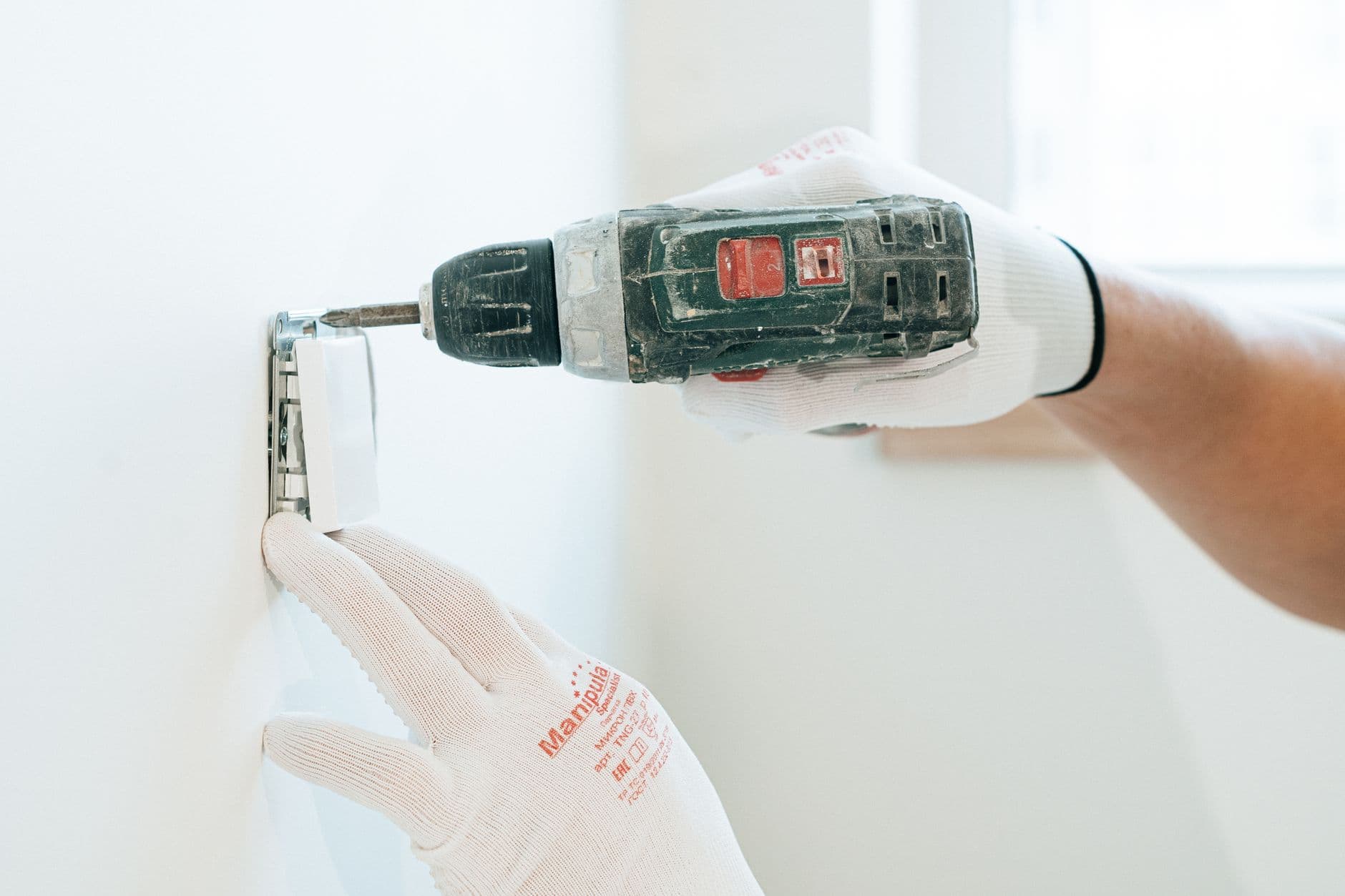 Elektricien met werkhandschoenen boort in een witte muur