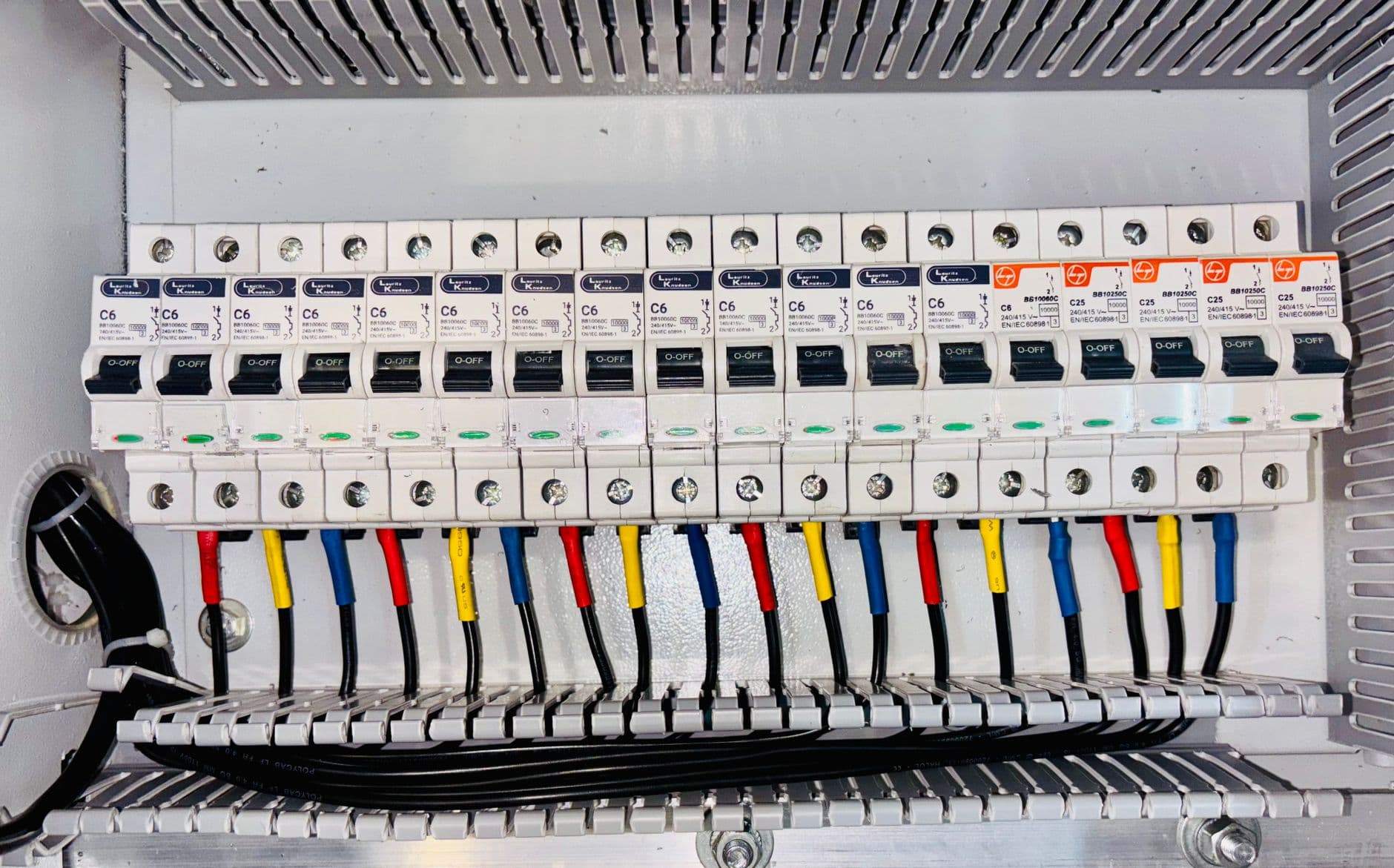 Tableau électrique ouvert avec une rangée de disjoncteurs et un câblage codé par couleur