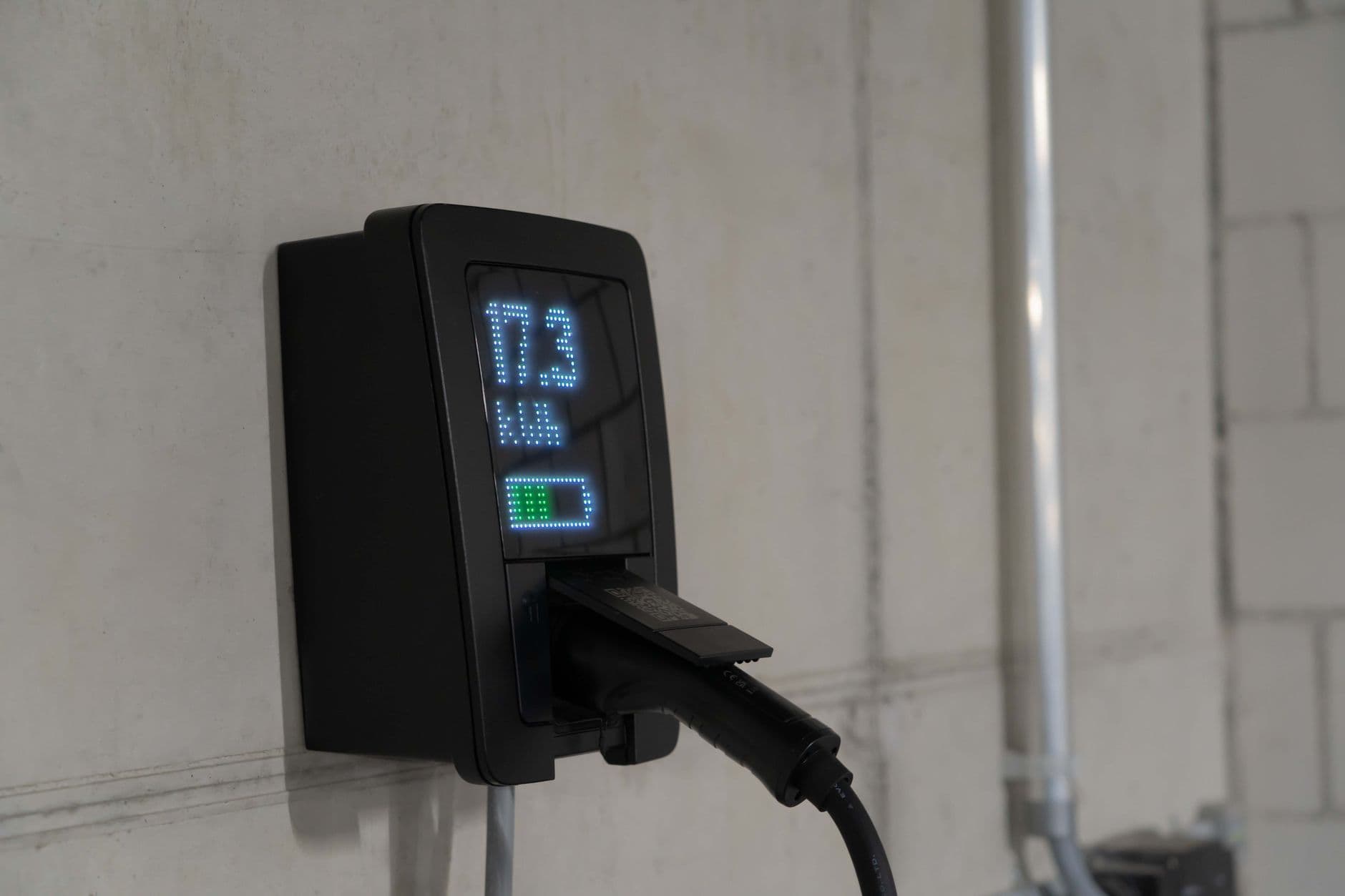 Black wall-mounted charger with a display and plugged-in connector in a garage