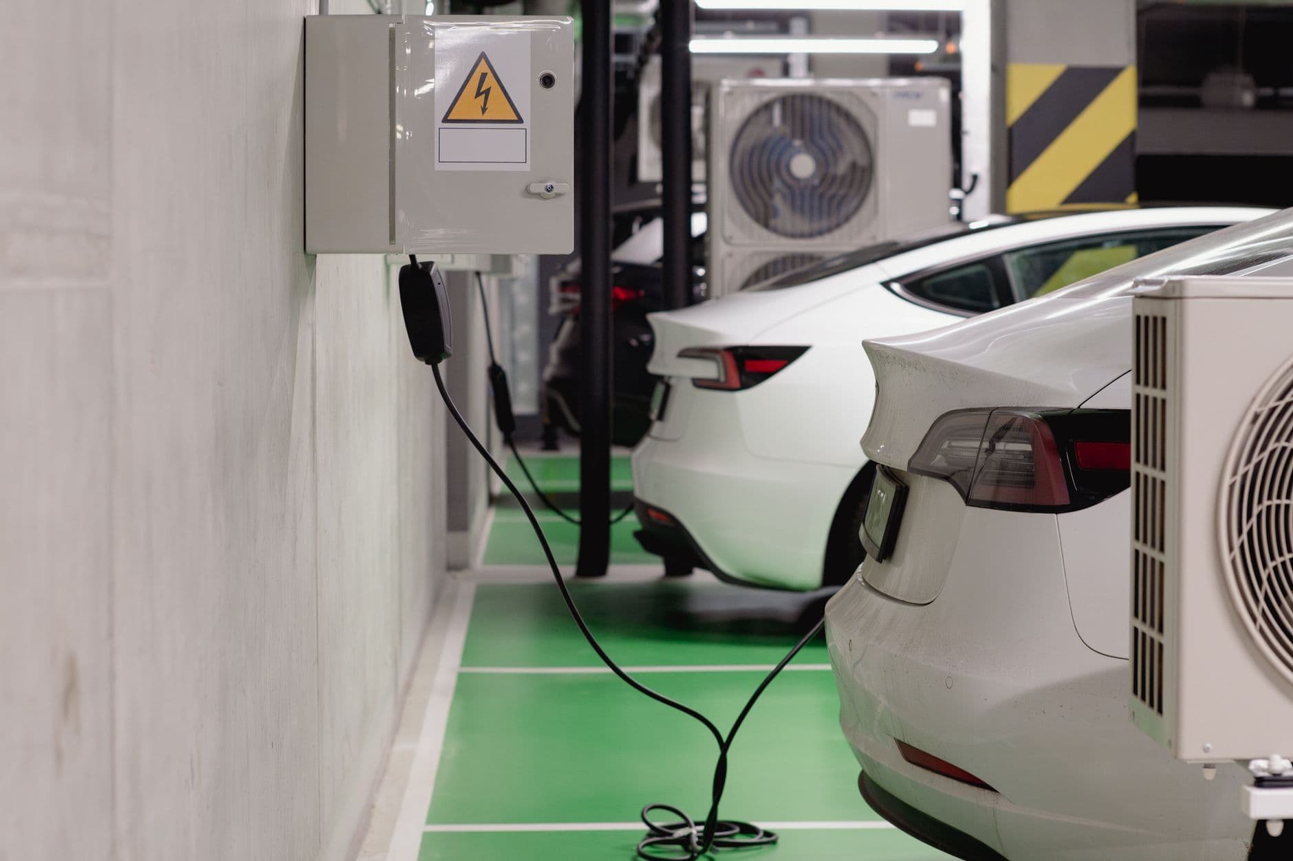 Deux voitures électriques en charge dans un parking souterrain, reliées à un coffret électrique mural