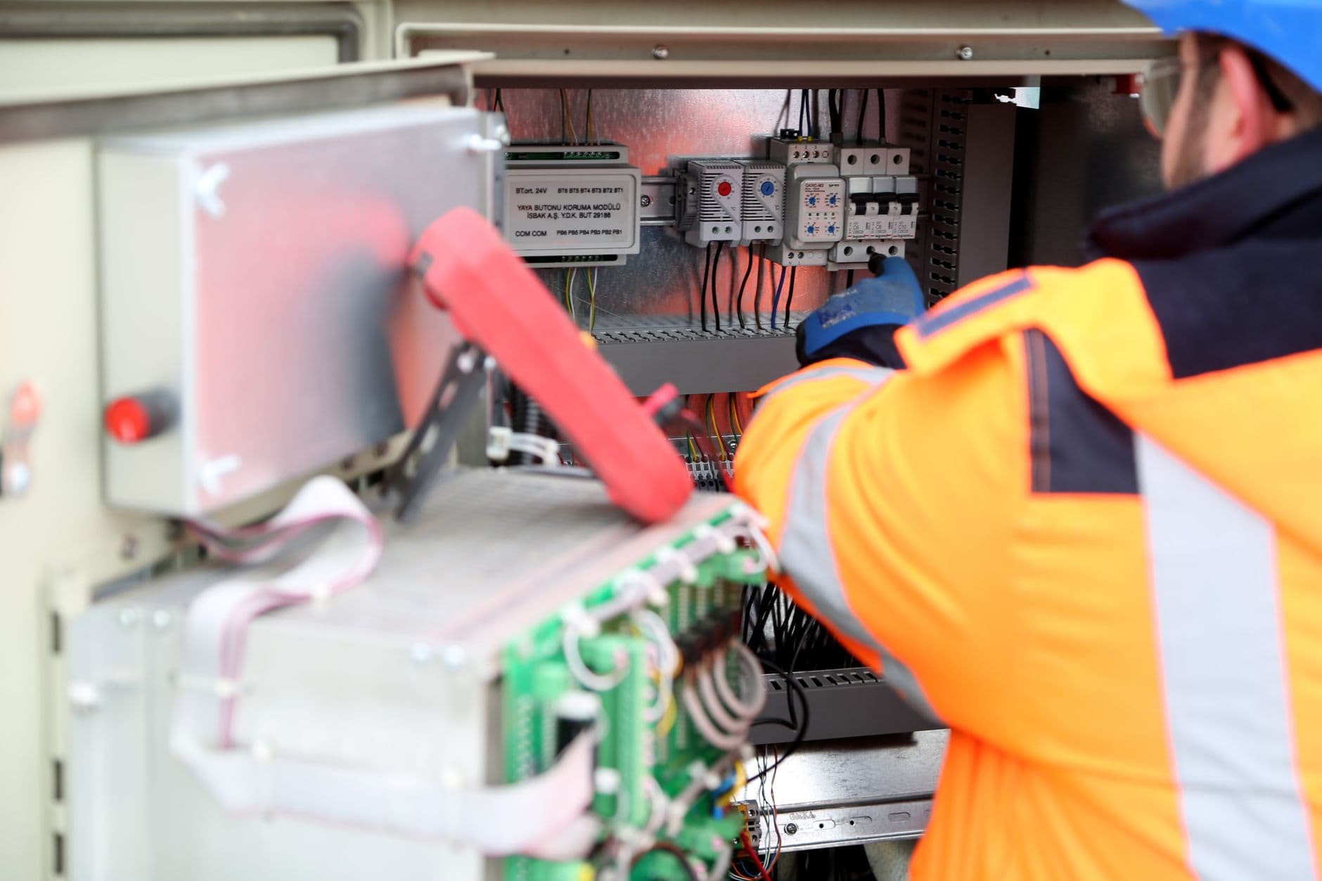 Technician with gloves using a measuring tool on an open cabinet with electronics