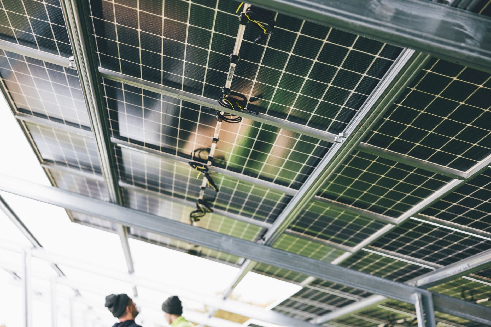 Onderkant van zonnepanelen met bekabeling en stekkerverbindingen, twee installateurs eronder