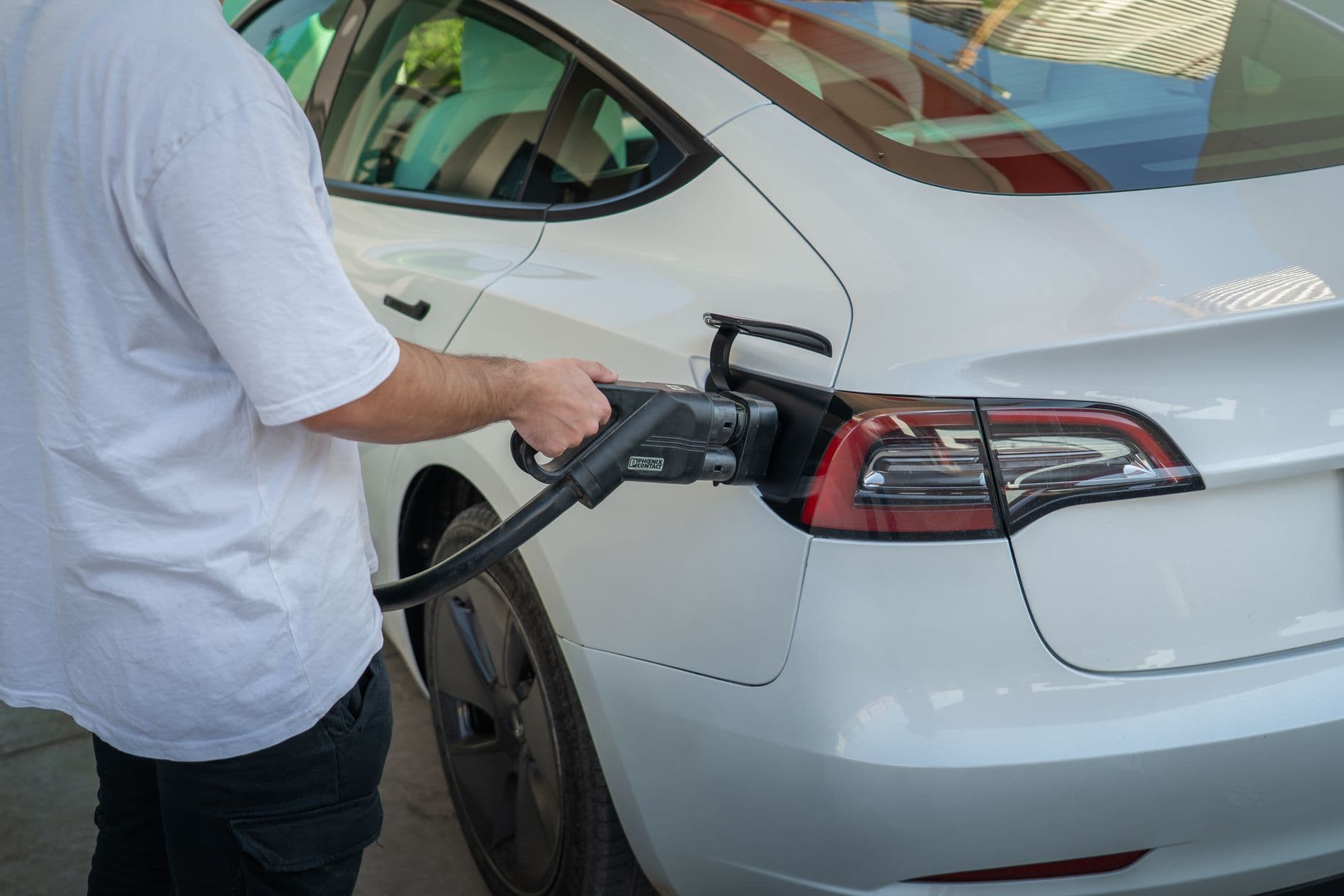 Iemand steekt de laadkabel in een witte elektrische auto