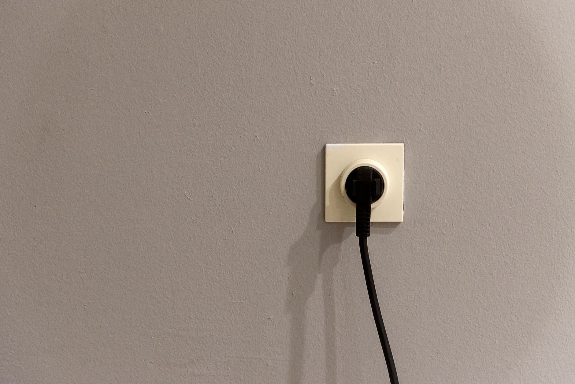 Black plug inserted into a wall socket on a grey wall
