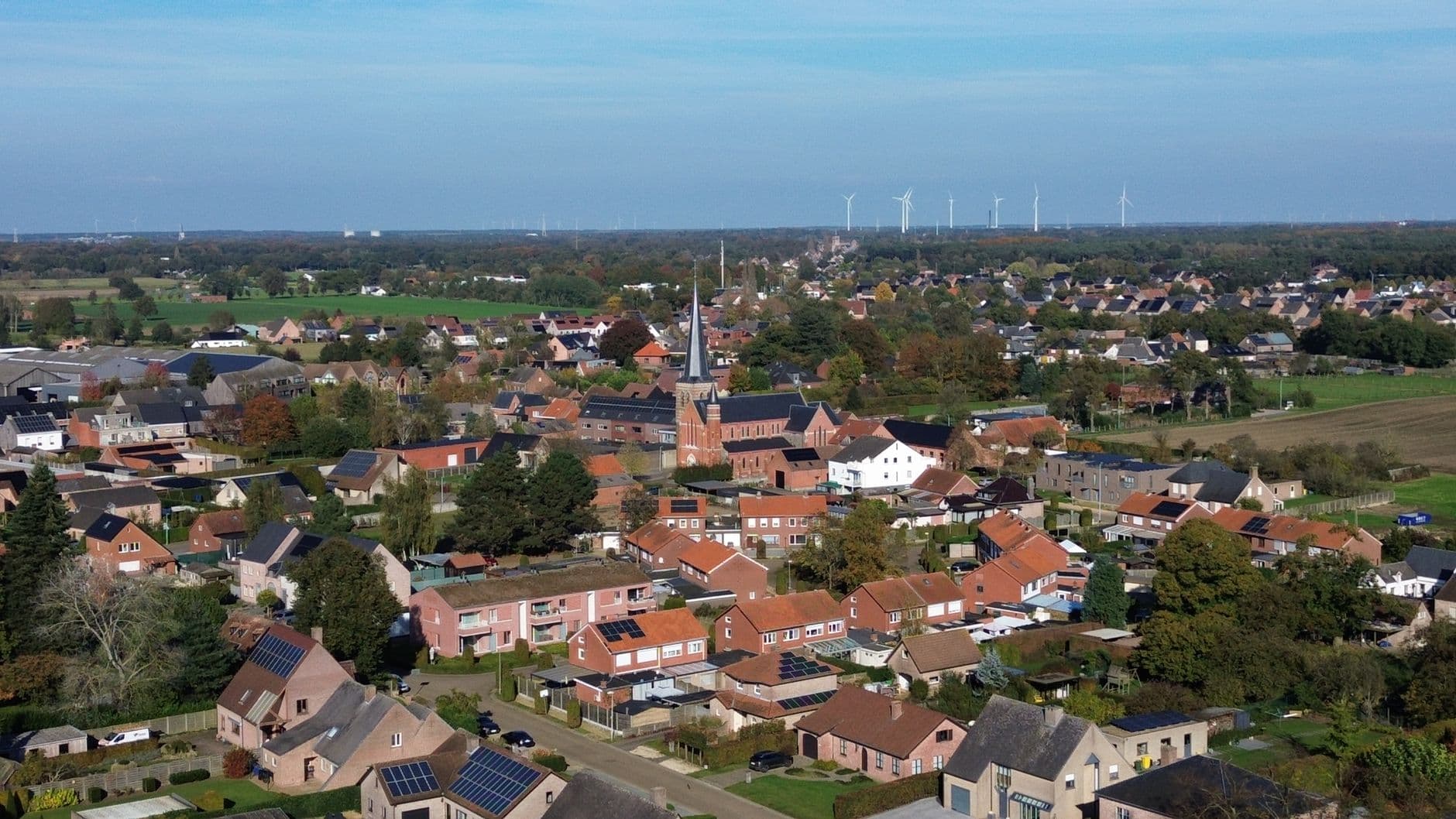 Vue aérienne d'un village flamand avec des maisons autour de l'église et des éoliennes à l'horizon