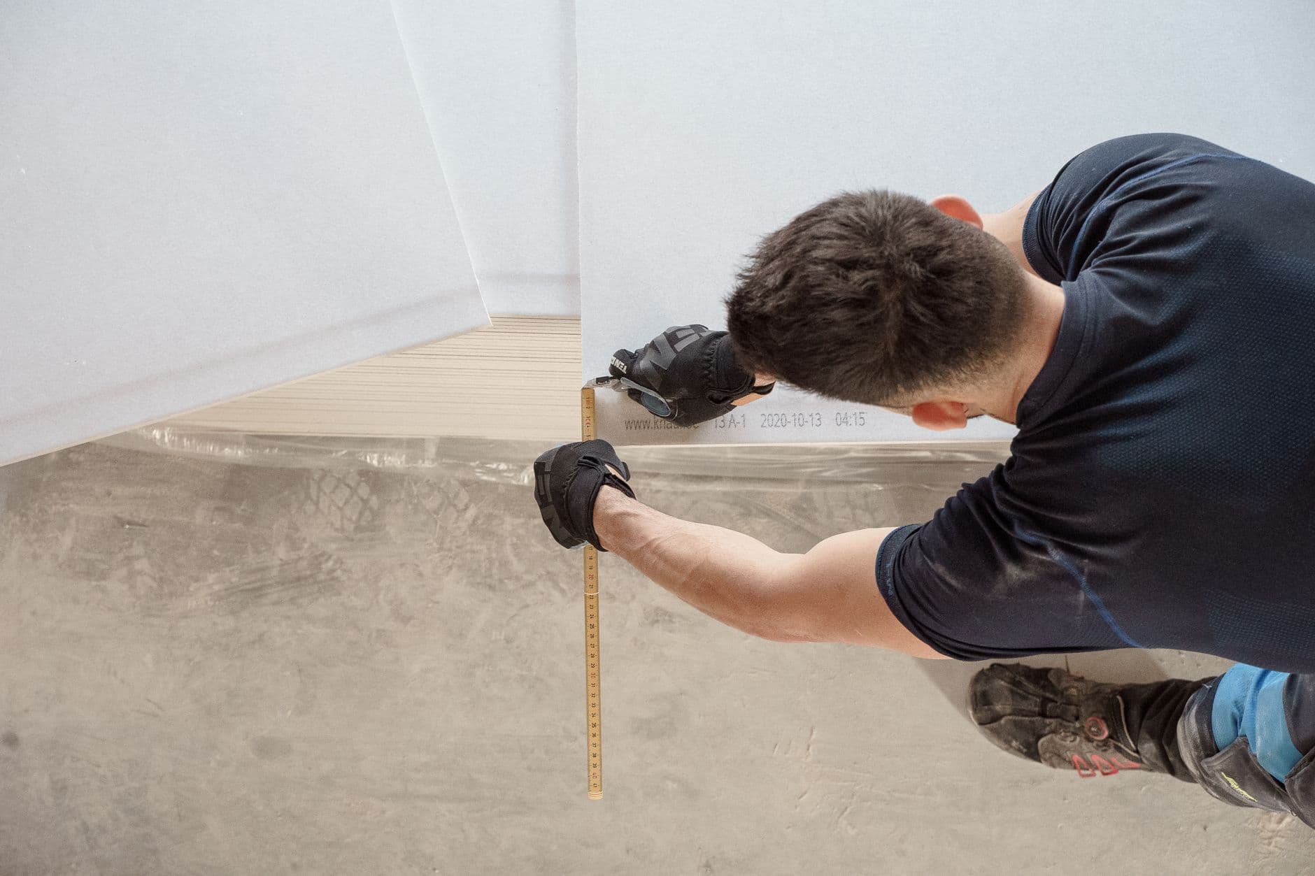 Artisan avec gants utilisant un mètre ruban sur une dalle en béton recouverte de film